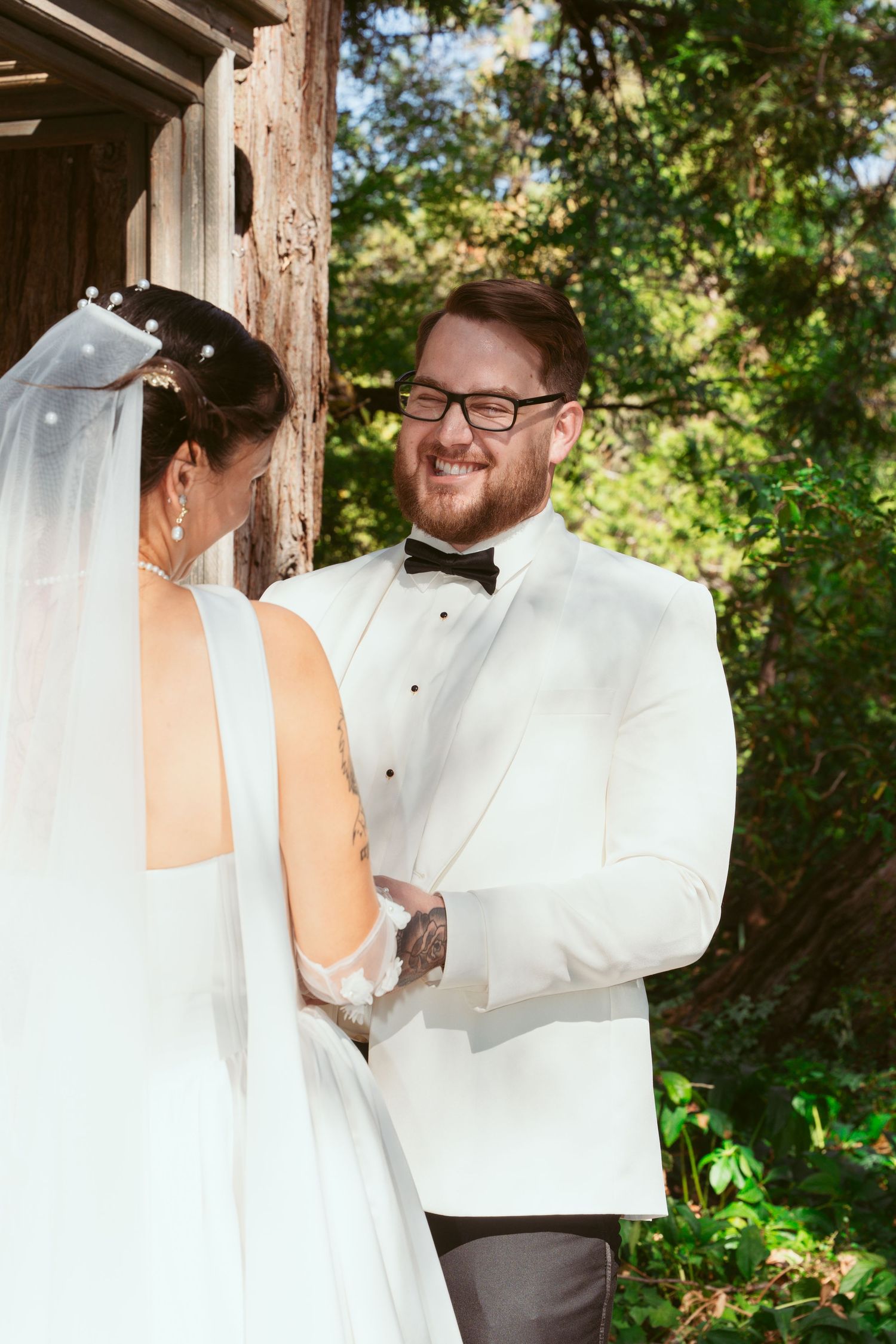 An intimate wedding ceremony moment captured under a rustic wooden pergola in a garden setting.