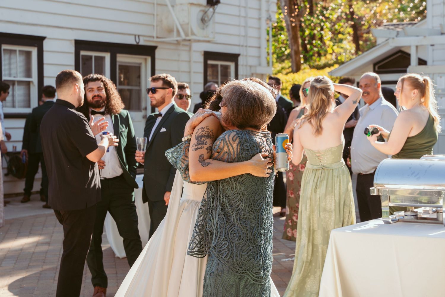 Wedding party members dancing outdoors in formal attire with green bridesmaid dresses and dark suits.