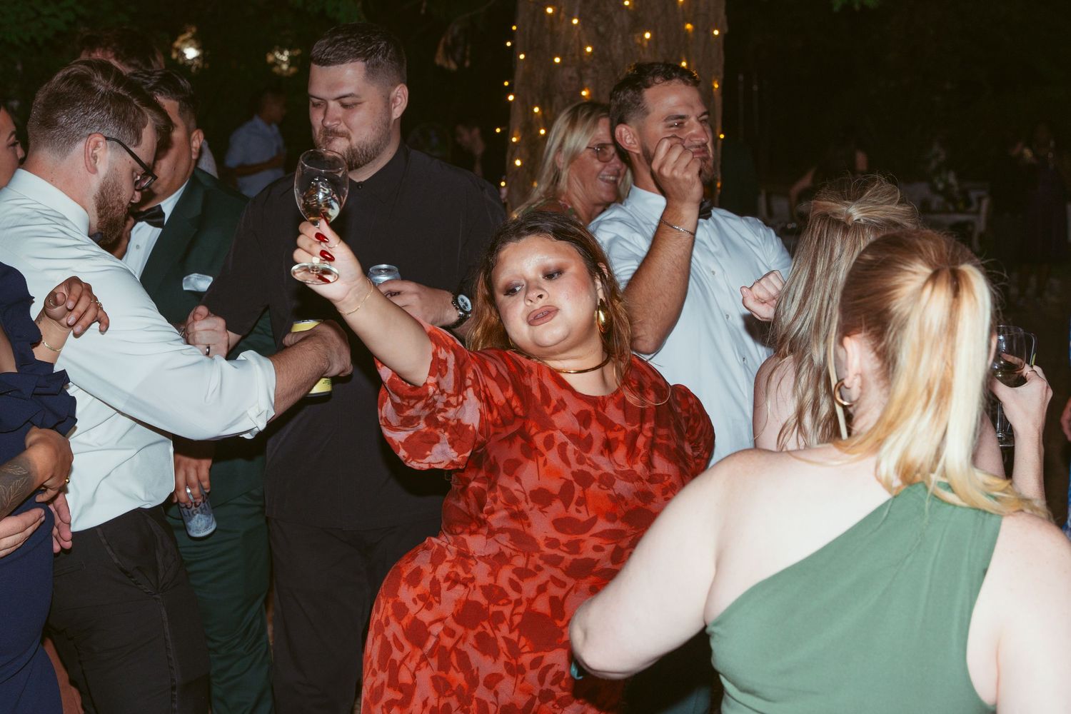 Guests dancing and celebrating at a nighttime wedding reception under twinkling lights.