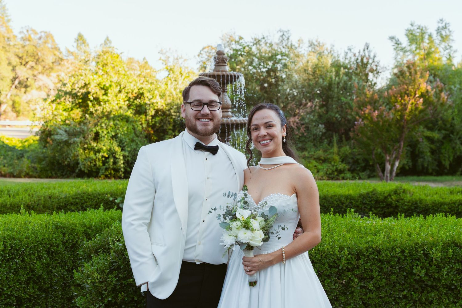 A couple poses for formal wedding portraits in a manicured garden setting.