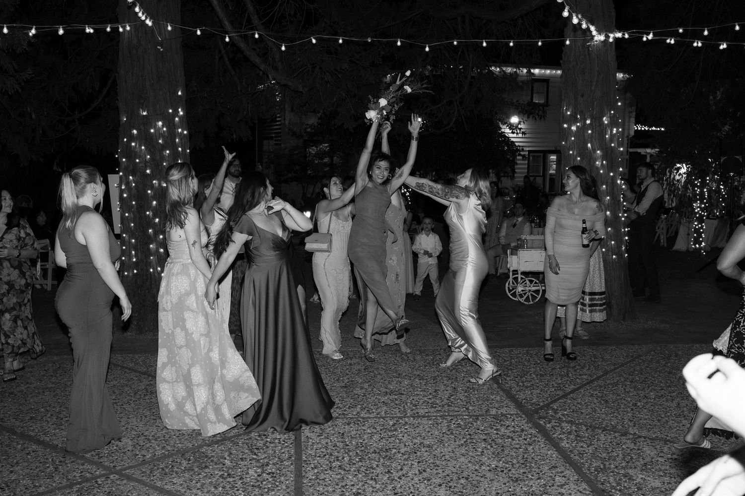 Wedding guests dance and celebrate on an outdoor dance floor under string lights at night.