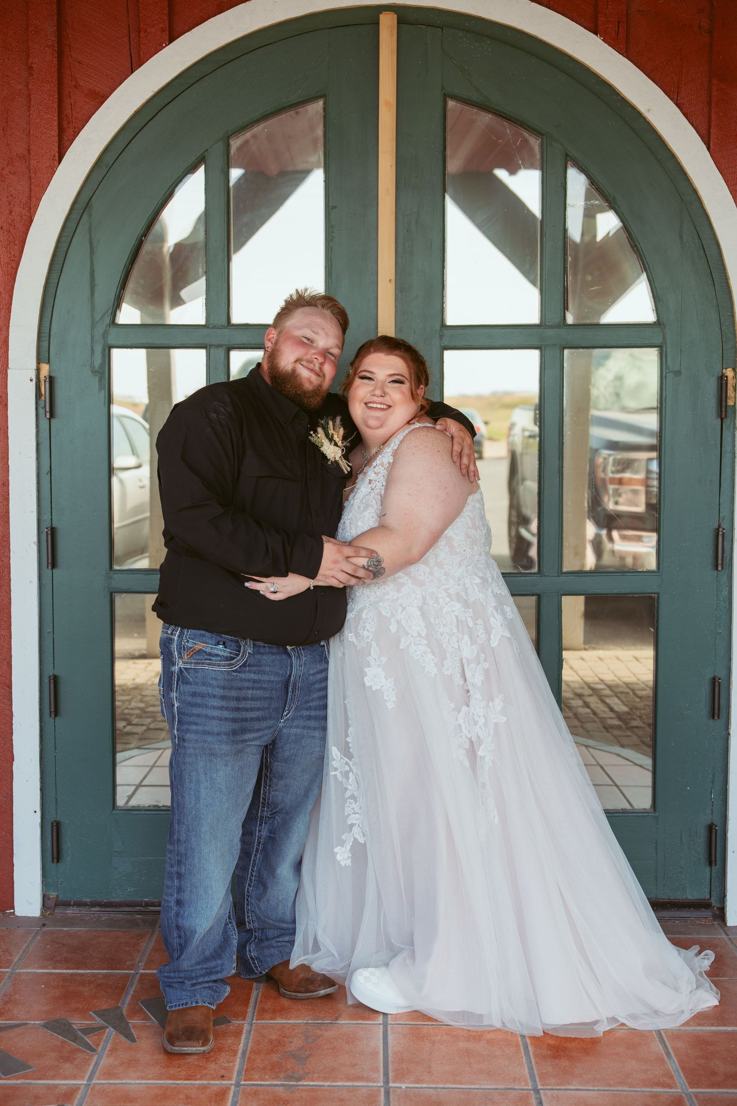 Couple shares playful poses in sequence against red building with teal arched doors.