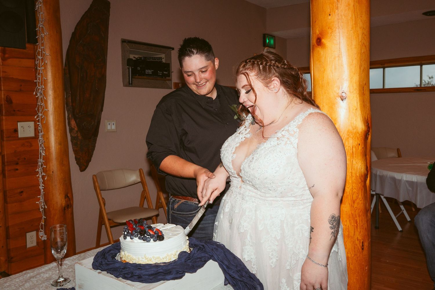 Wedding celebration inside a rustic wooden lodge with log beam pillars.