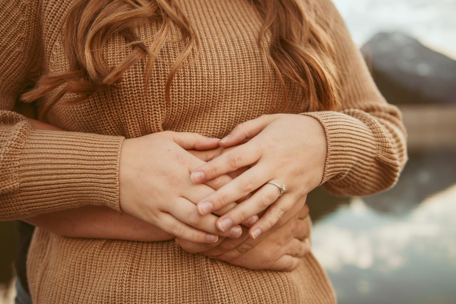 Detail shot of hands clasped together wearing a tan knit sweater.