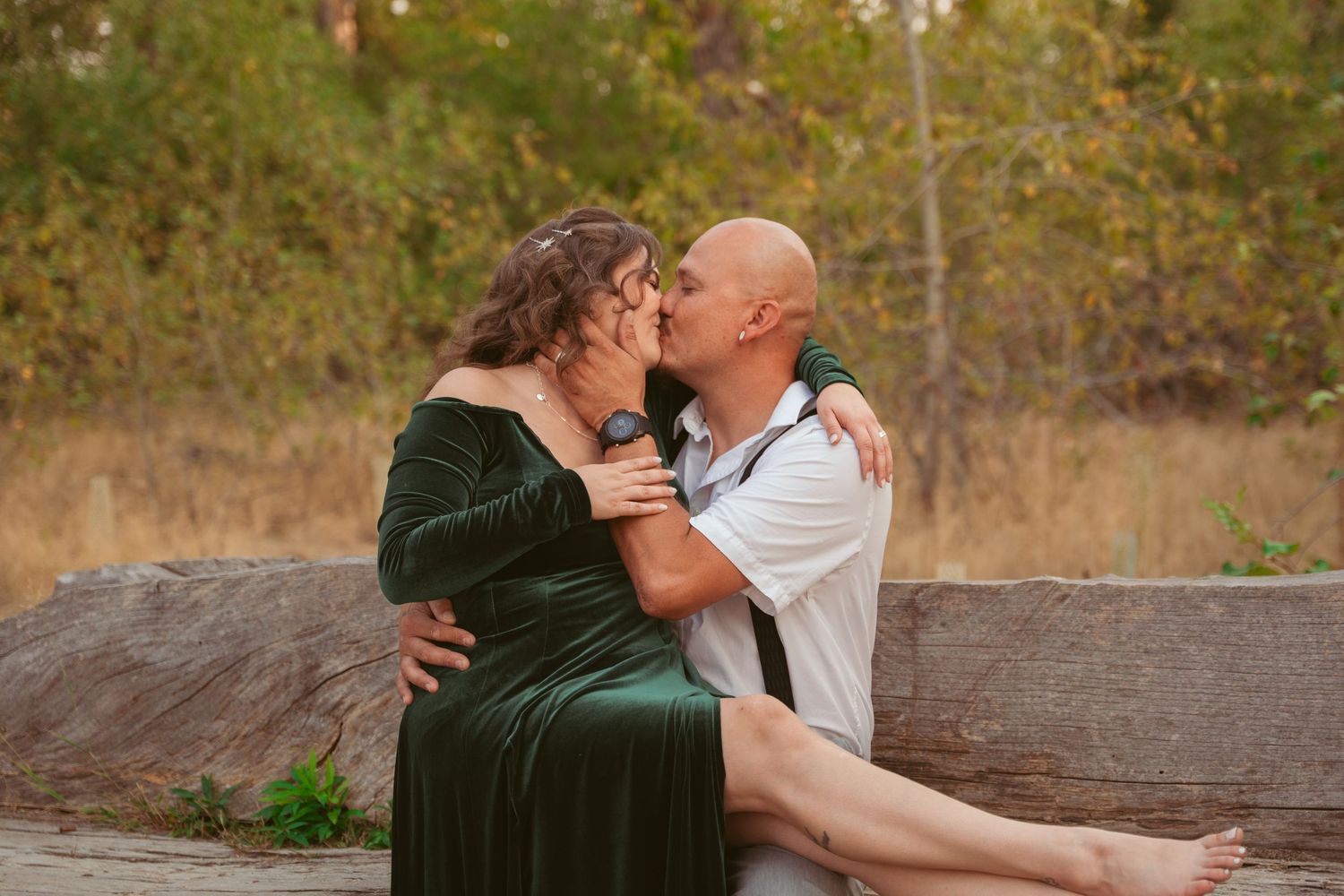 Couple sharing romantic moments on a rustic wooden bench outdoors.
