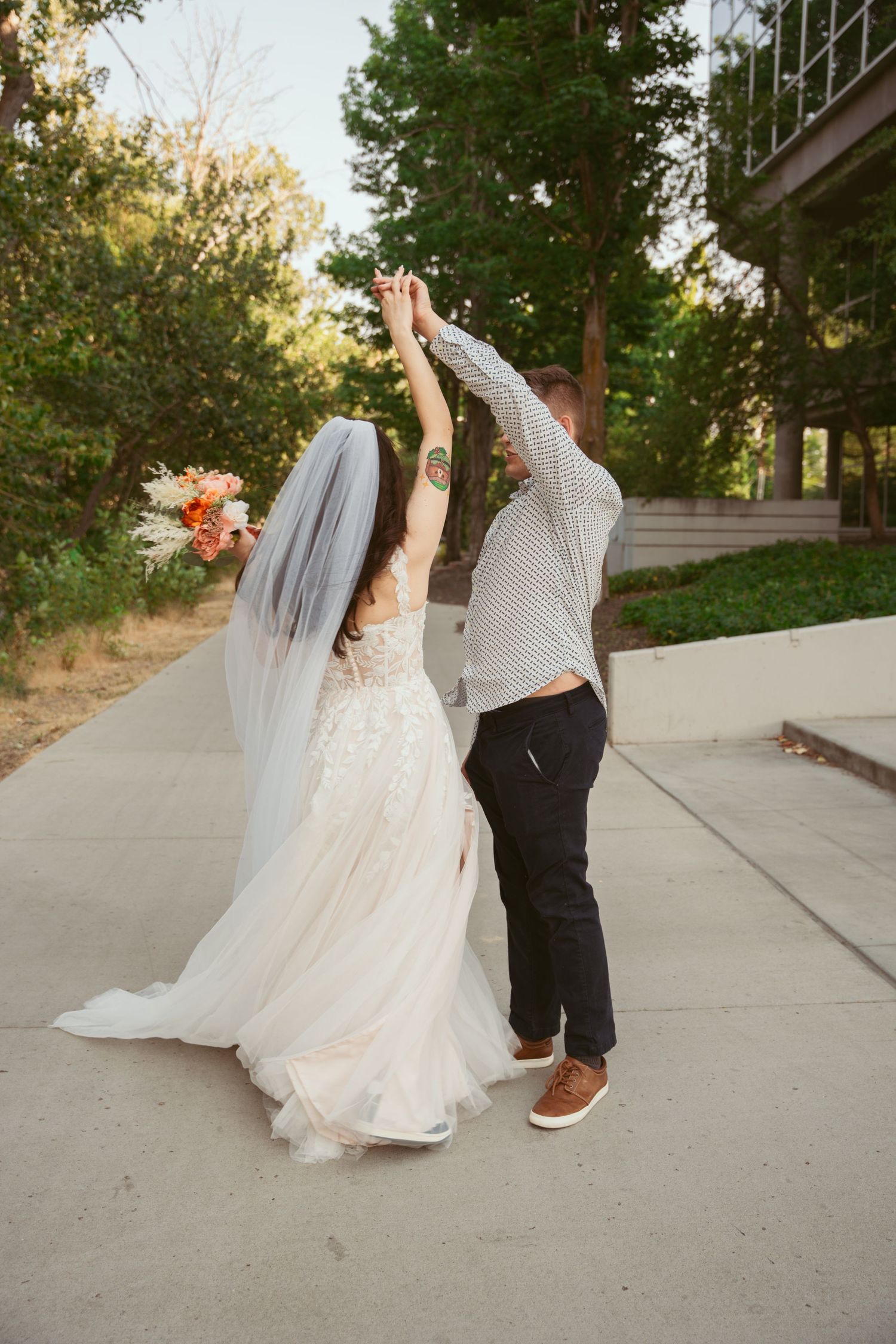 Playful dance sequence on concrete path with flowing white wedding dress in outdoor setting.