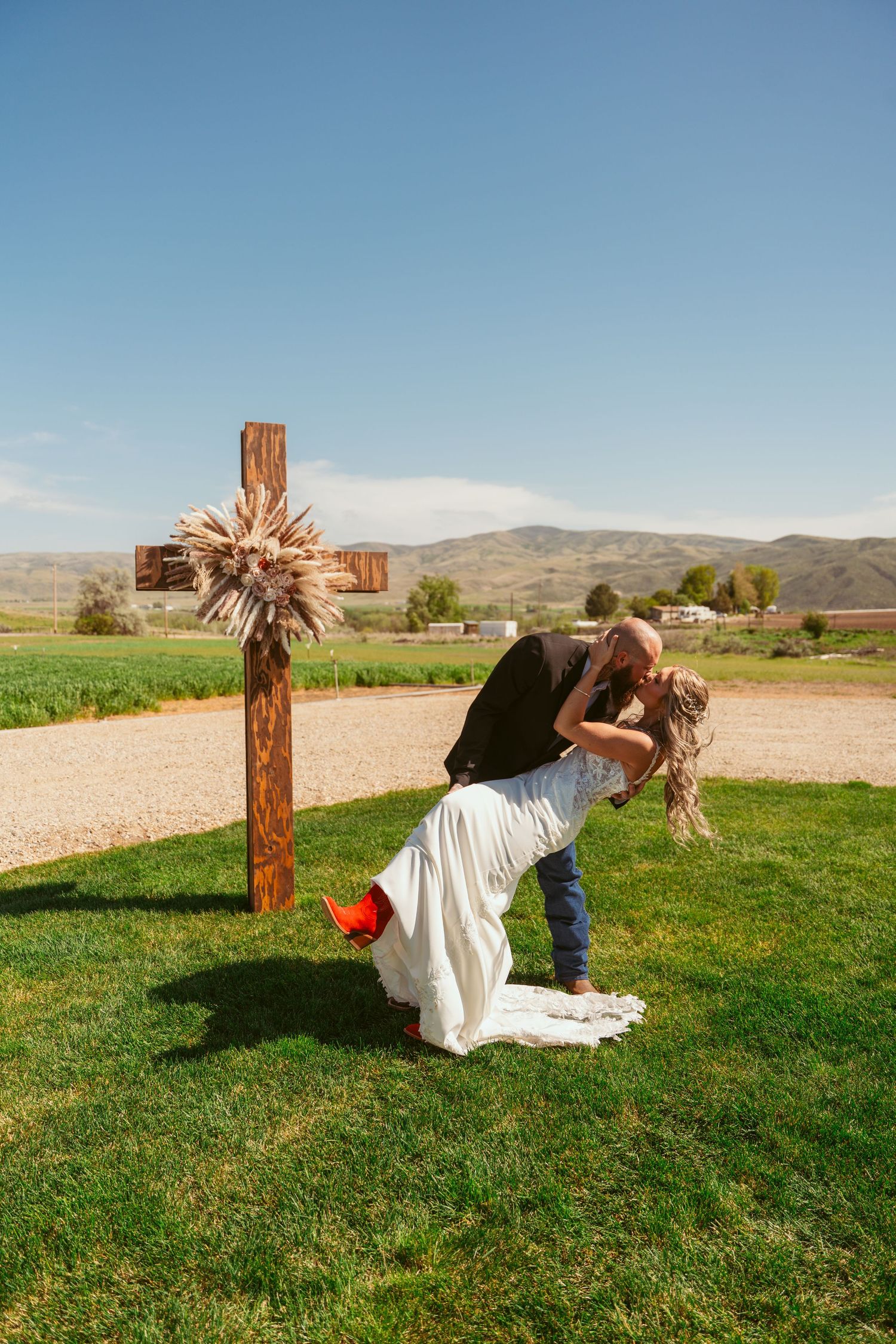 Newlyweds dance and dip dramatically on grass with wooden cross in background.