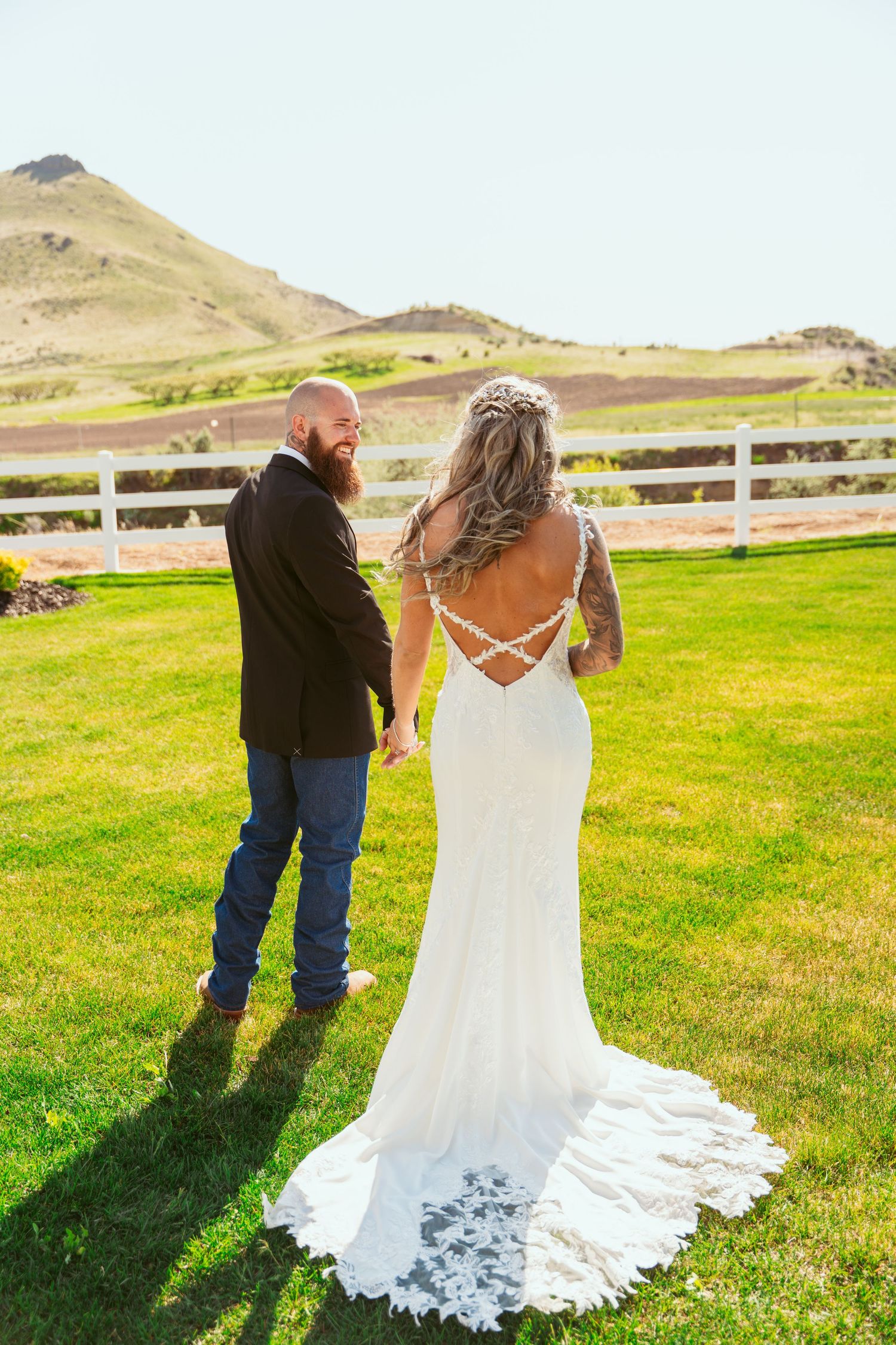 A couple poses for wedding photos in a scenic field with white fencing and mountain views.