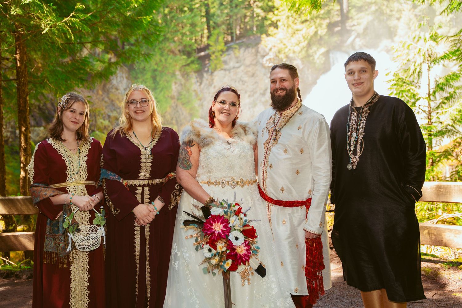 Wedding party in medieval attire poses together in front of a scenic forest backdrop.