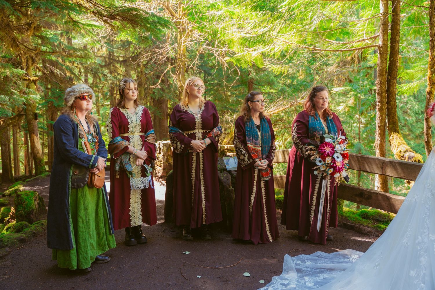 Wedding party members in medieval attire stand in formation during a forest ceremony.