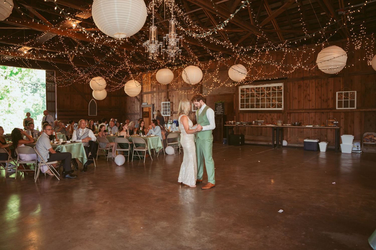 Wedding celebration dance in rustic barn setting with romantic lighting and decorative elements.