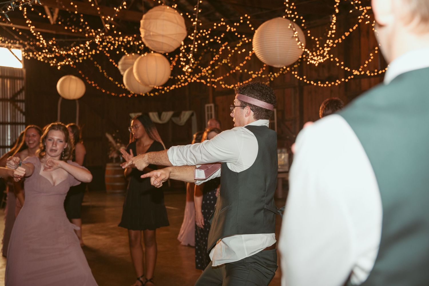 Wedding reception dance floor filled with guests under romantic lighting decor.