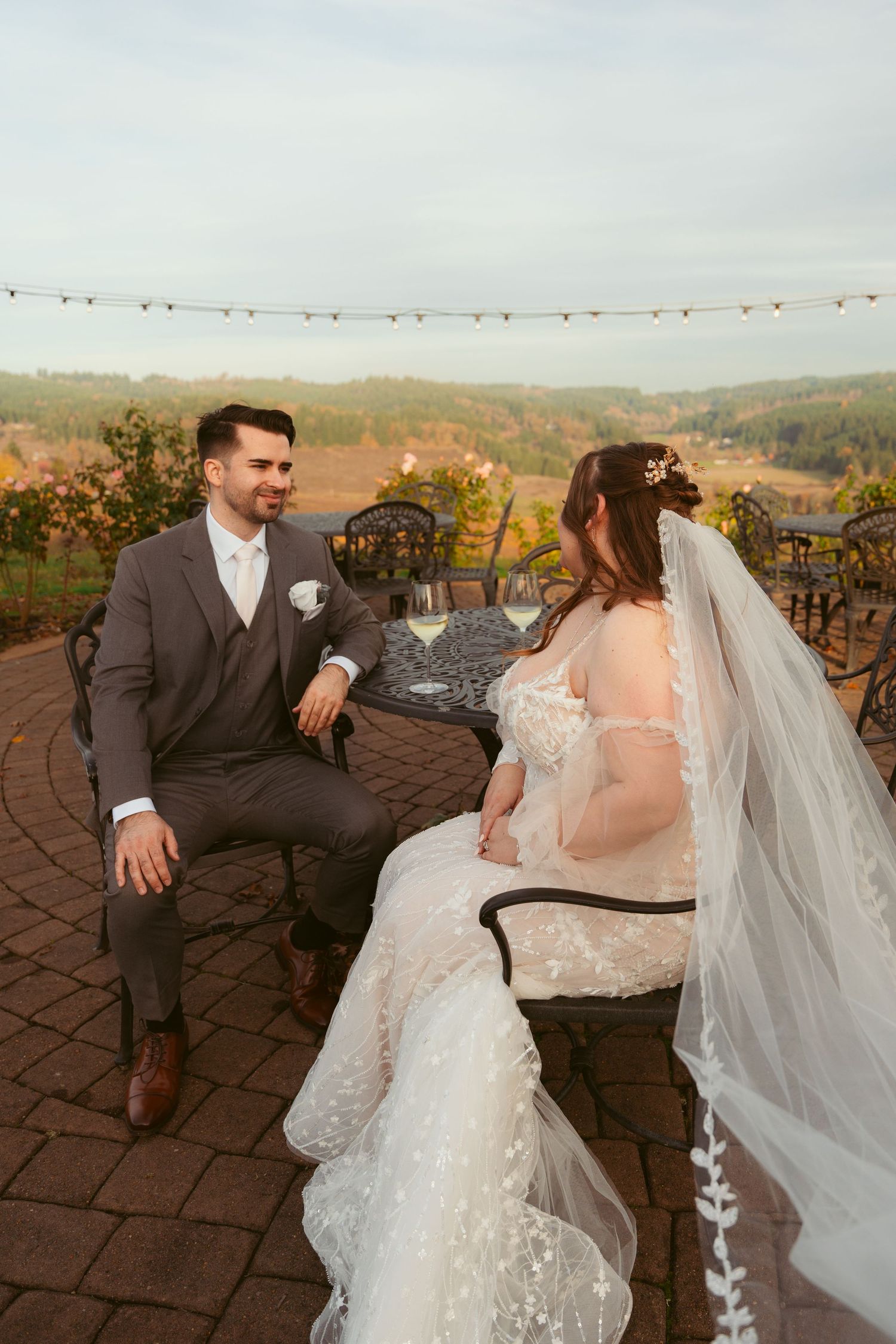 Newlyweds engage in conversation while seated at ornate patio furniture during golden hour.