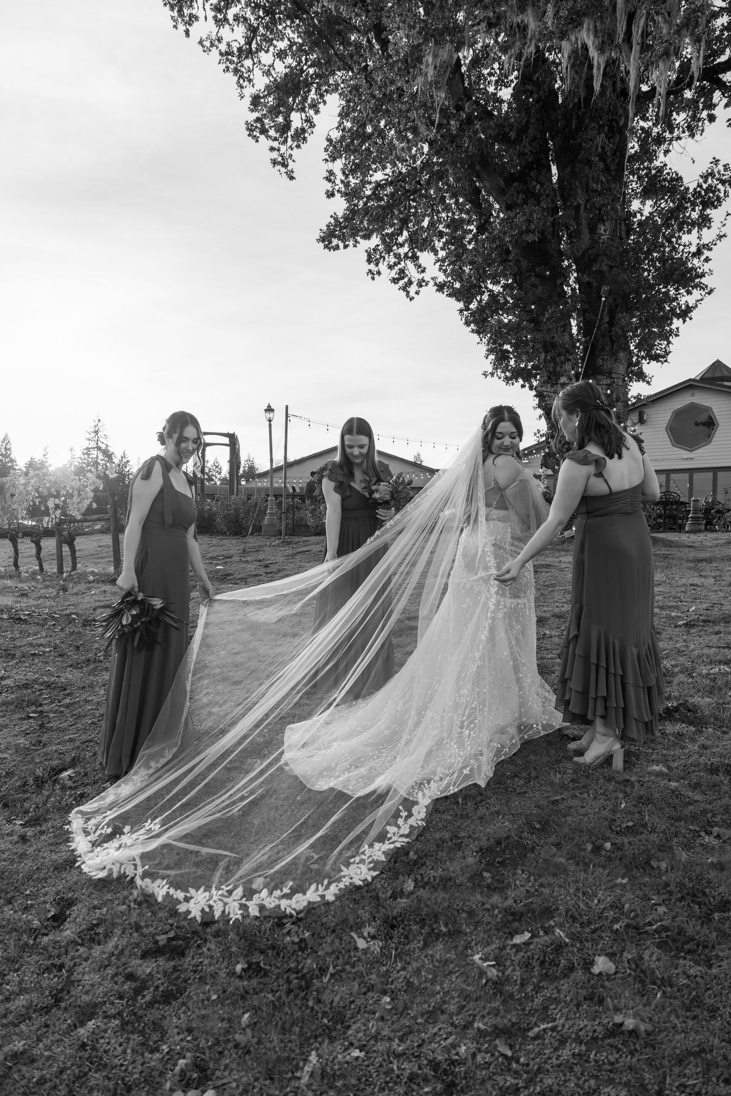 Black and white capture of wedding party arranging bride's long lace-trimmed veil.