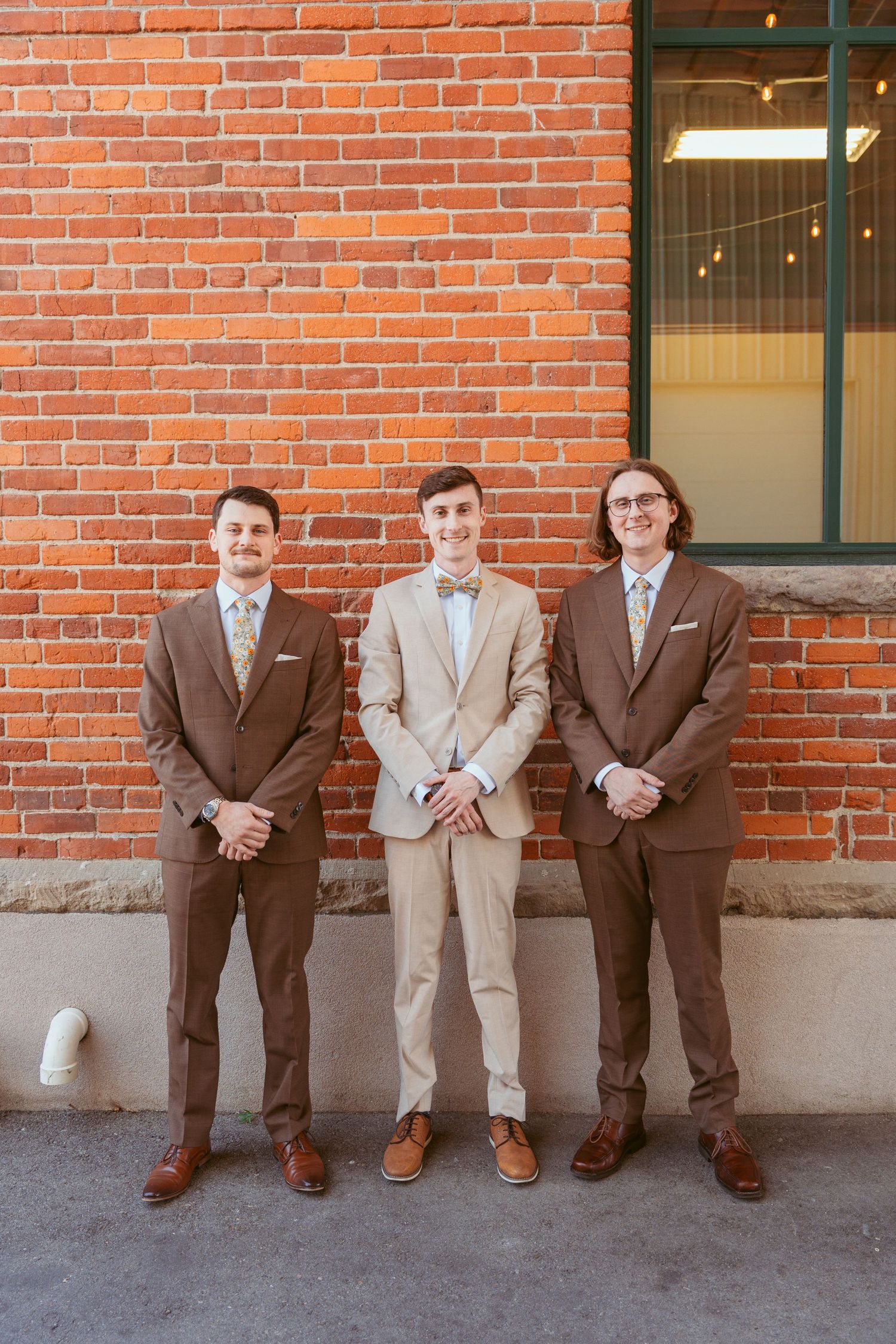 Groomsmen lined up against brick wall wearing brown and tan suits.