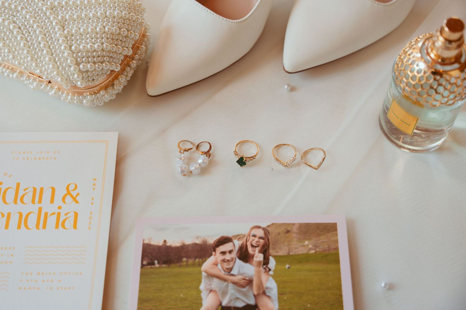 Wedding details including pearl accessories, rings, and gold-foiled stationery on white background.