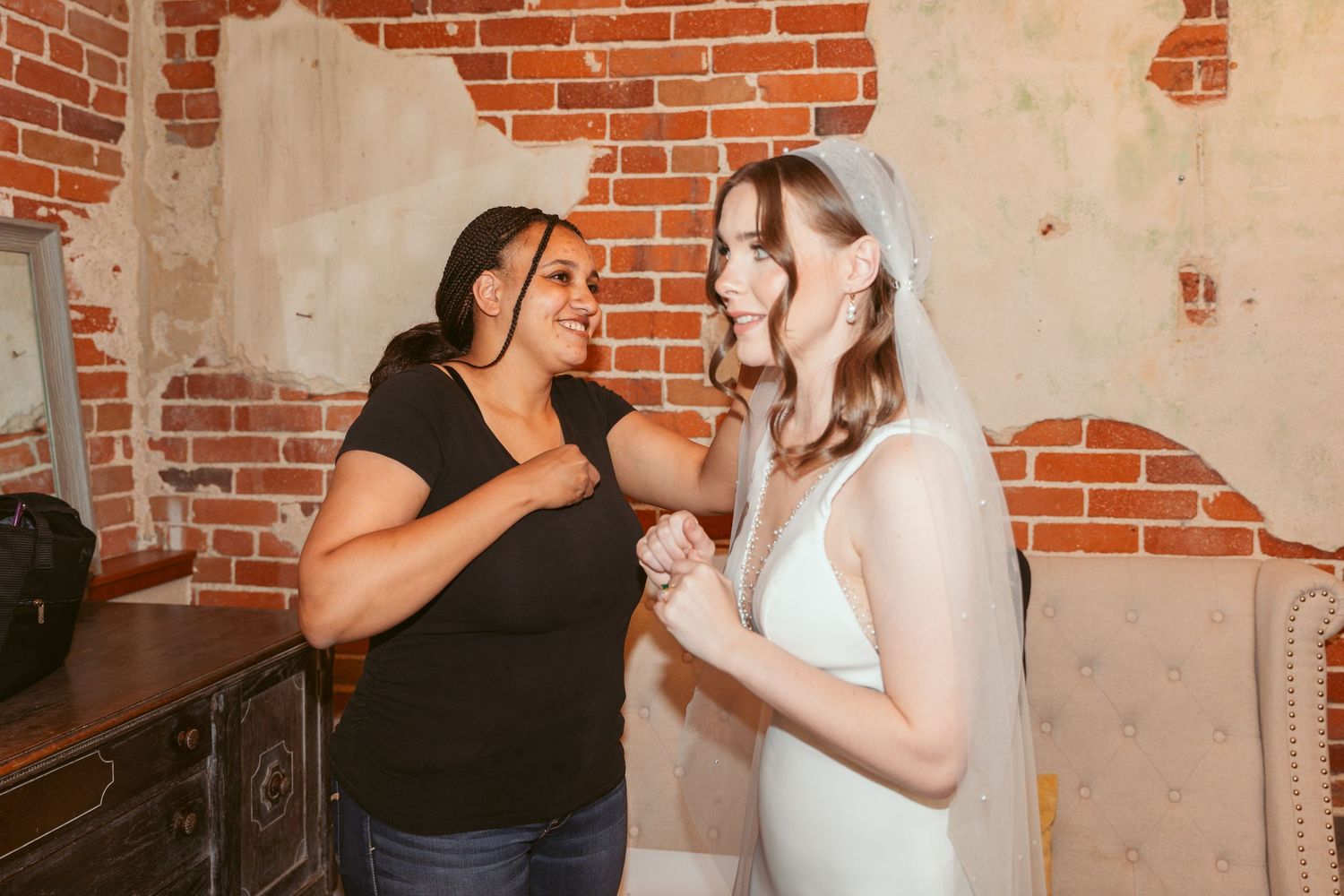 A makeup artist works on a client in a room with exposed brick walls and natural lighting.