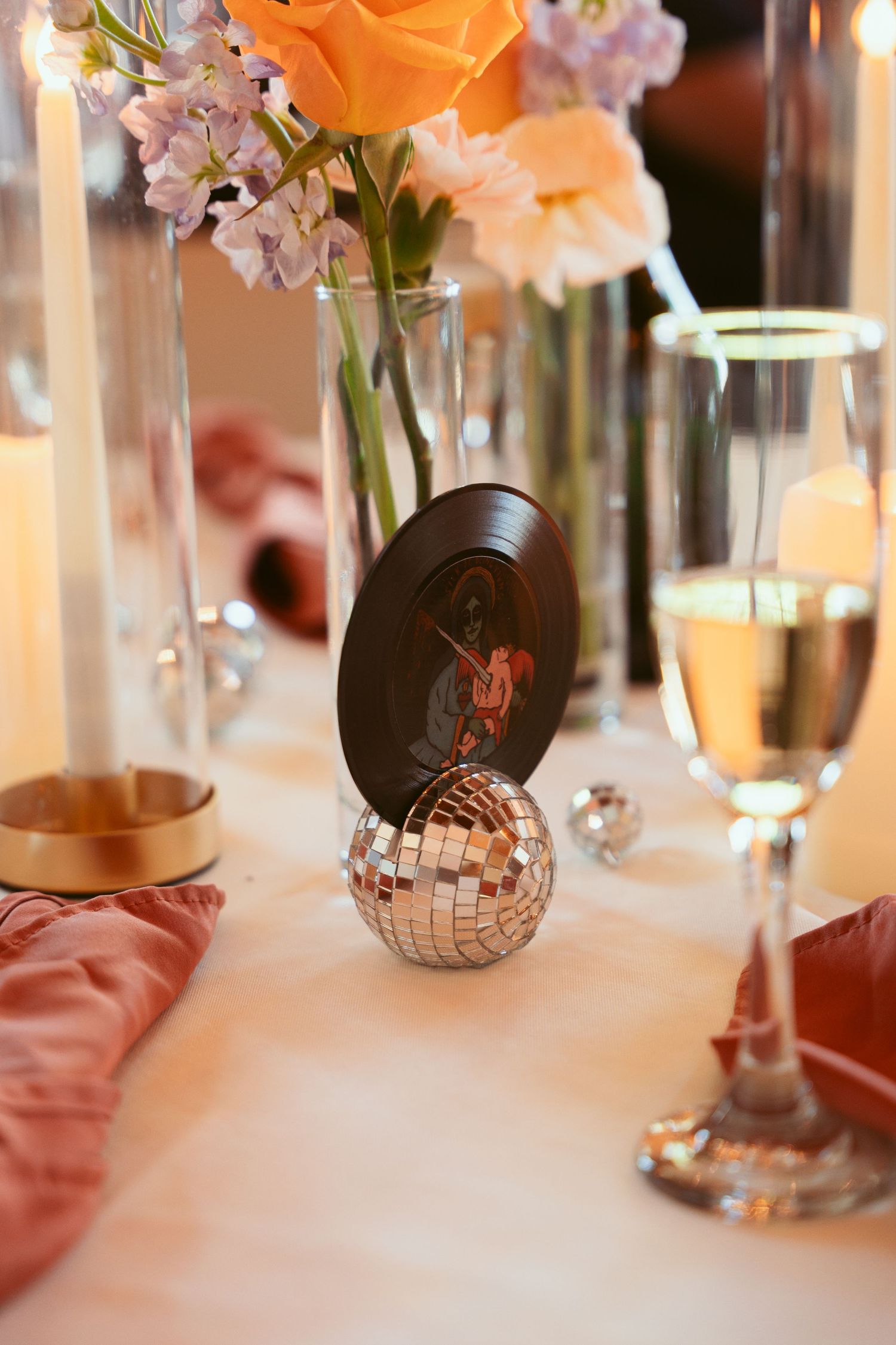 Wedding table centerpiece with orange roses, vinyl record, and disco ball detail.