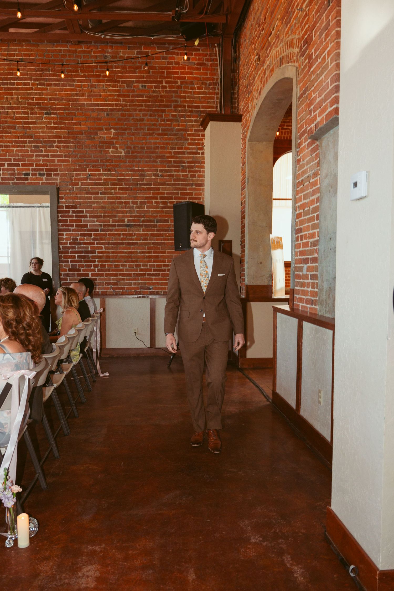 Long view of rustic brick wedding venue showing architectural details and guest seating.