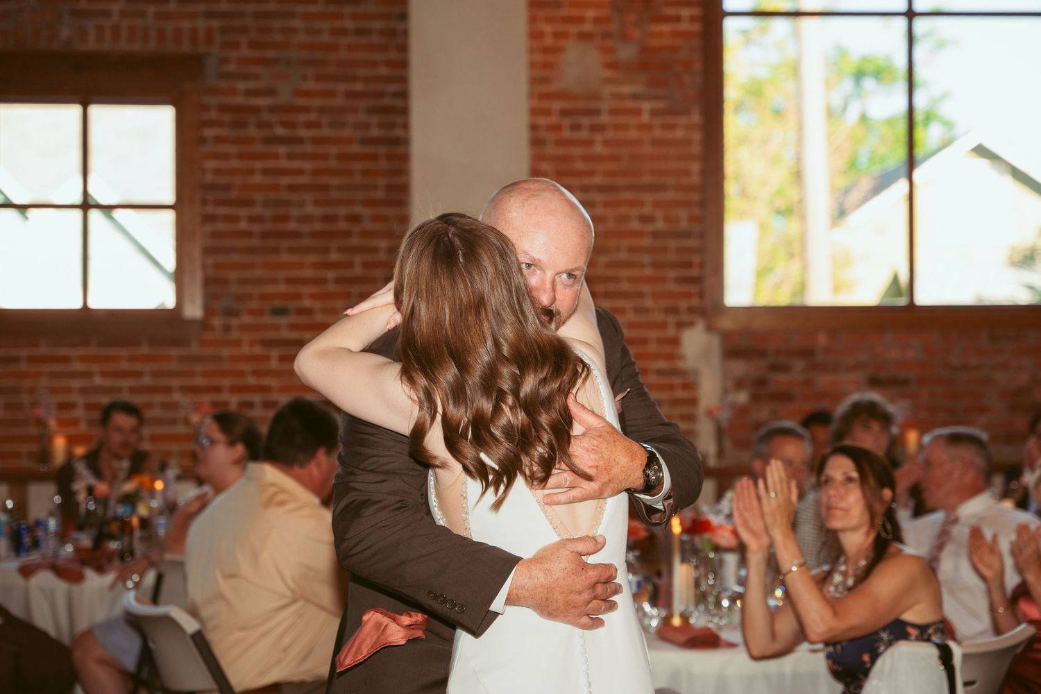 Wedding reception dance floor scene in a sunlit brick venue.