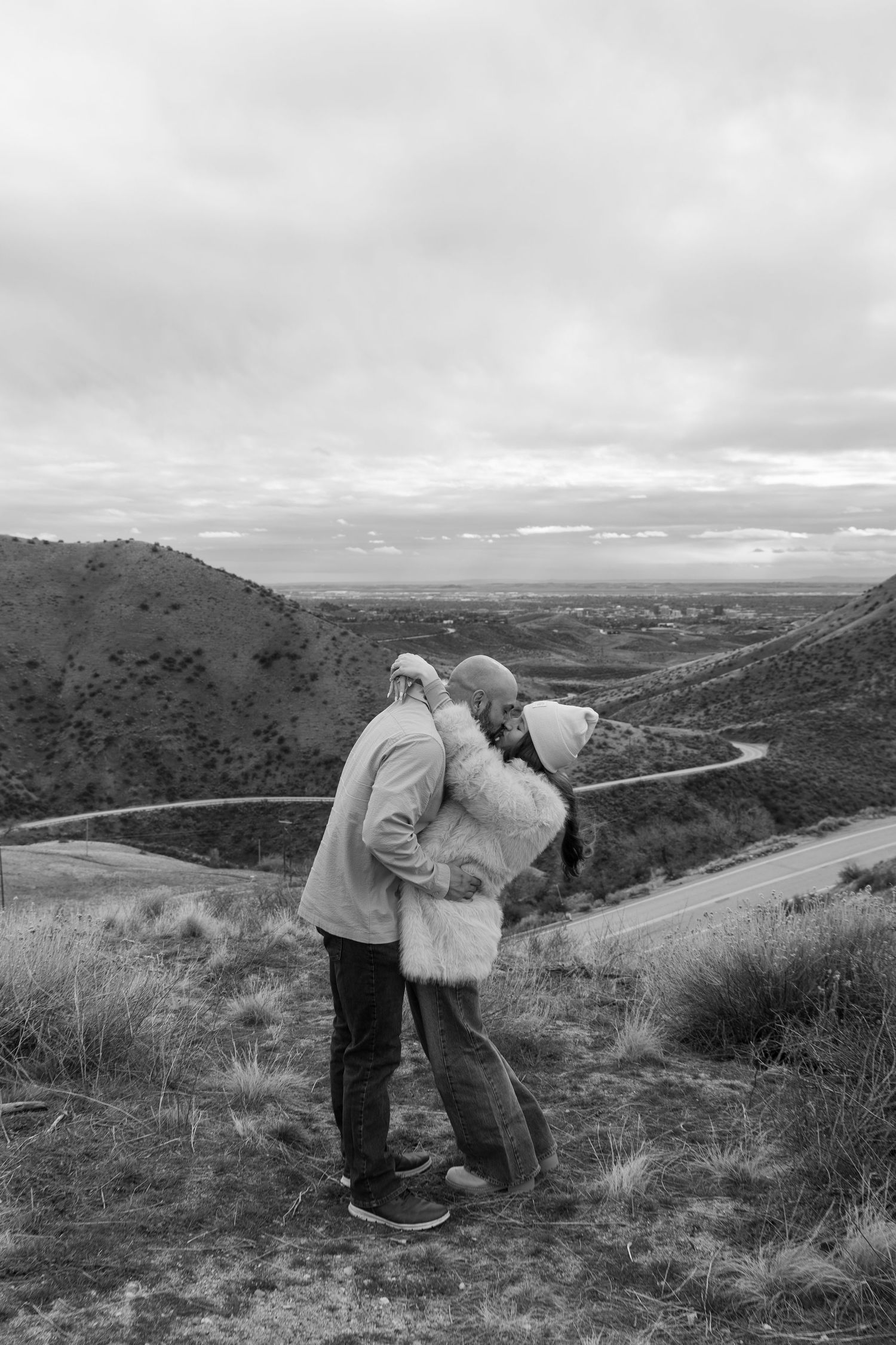 Romantic couple embracing on hilltop overlooking scenic mountain landscape.