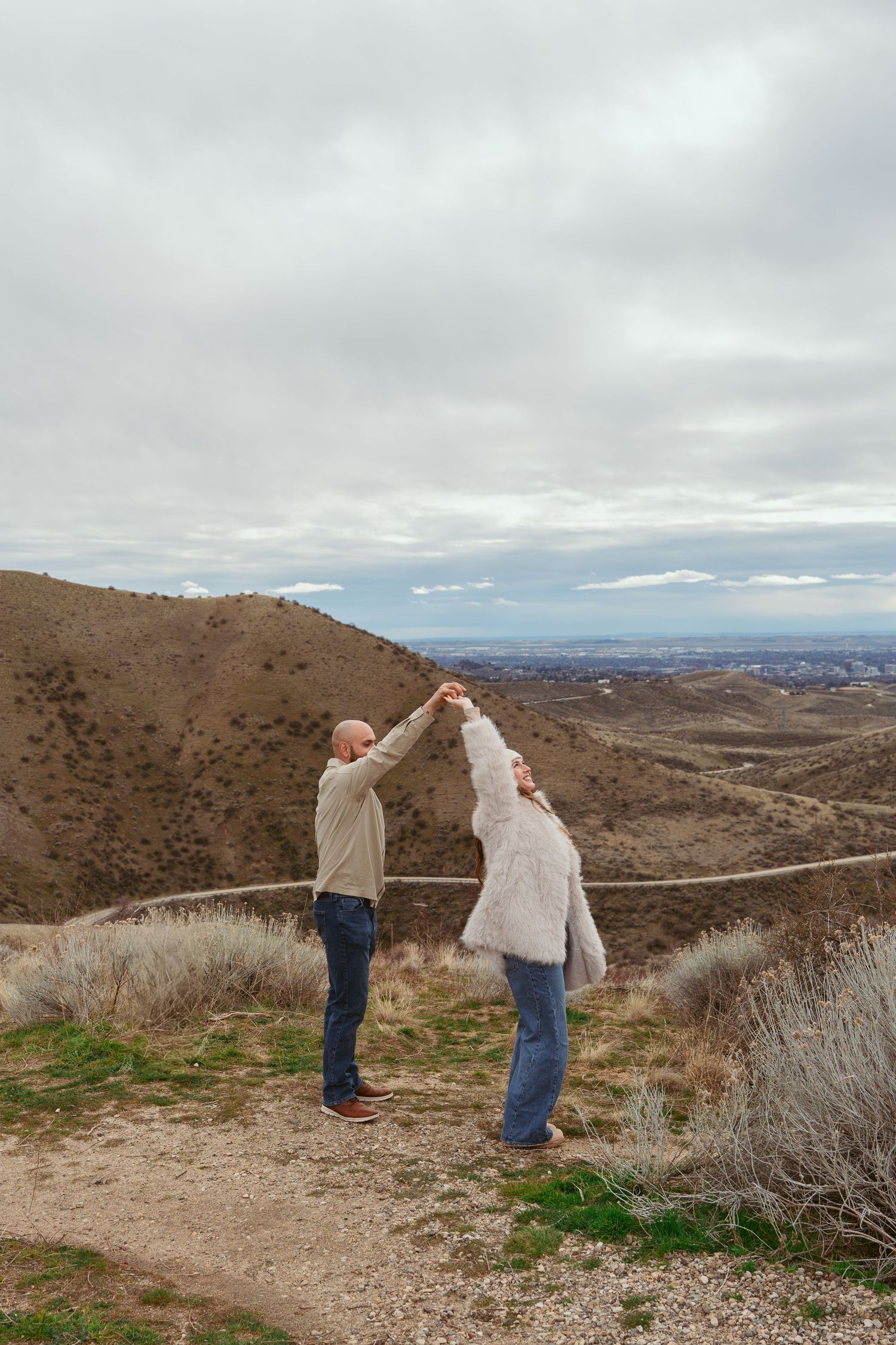 Couple dancing together on hiking trail with panoramic mountain vista in background.