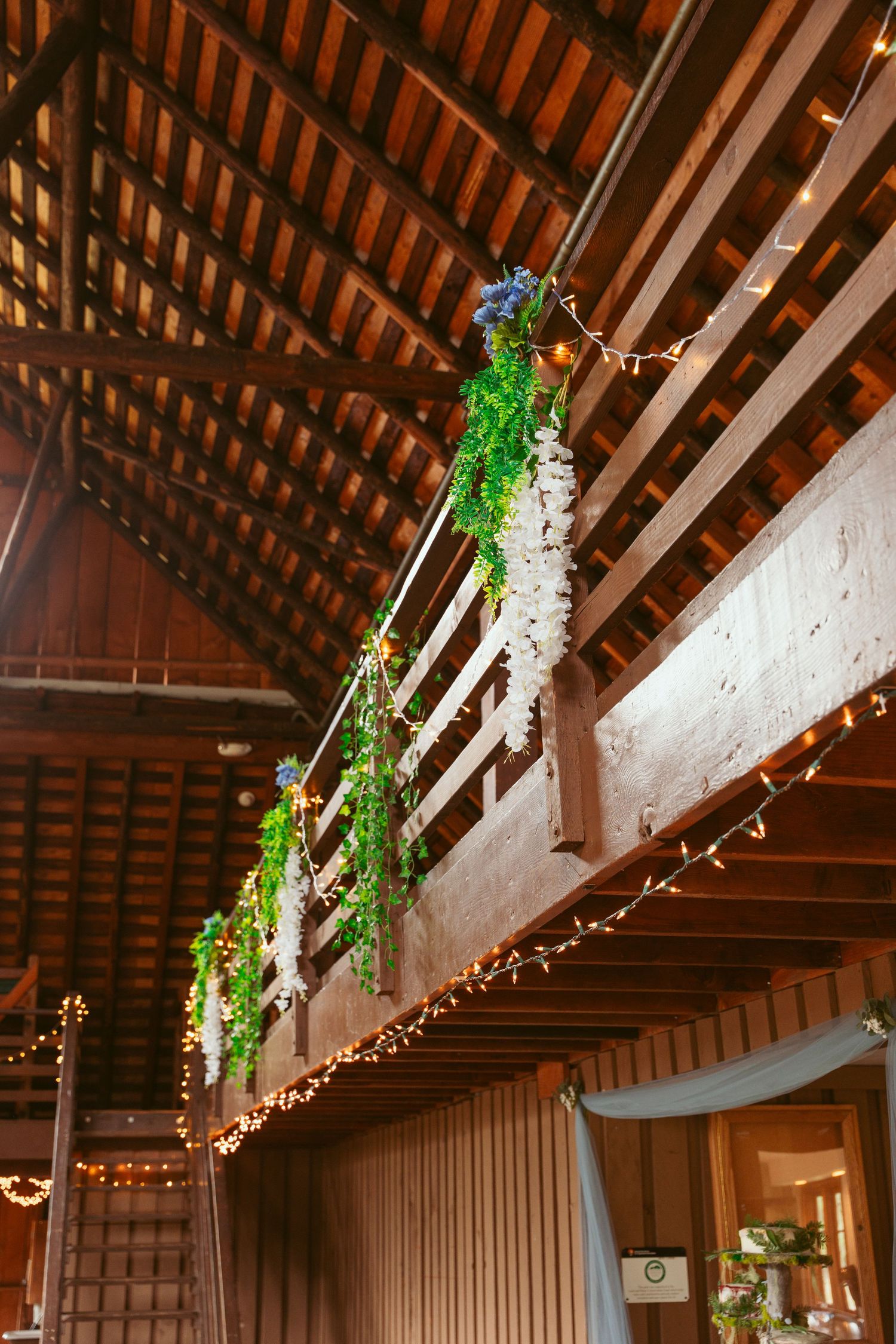 Hanging floral arrangements and string lights adorn wooden barn rafters.