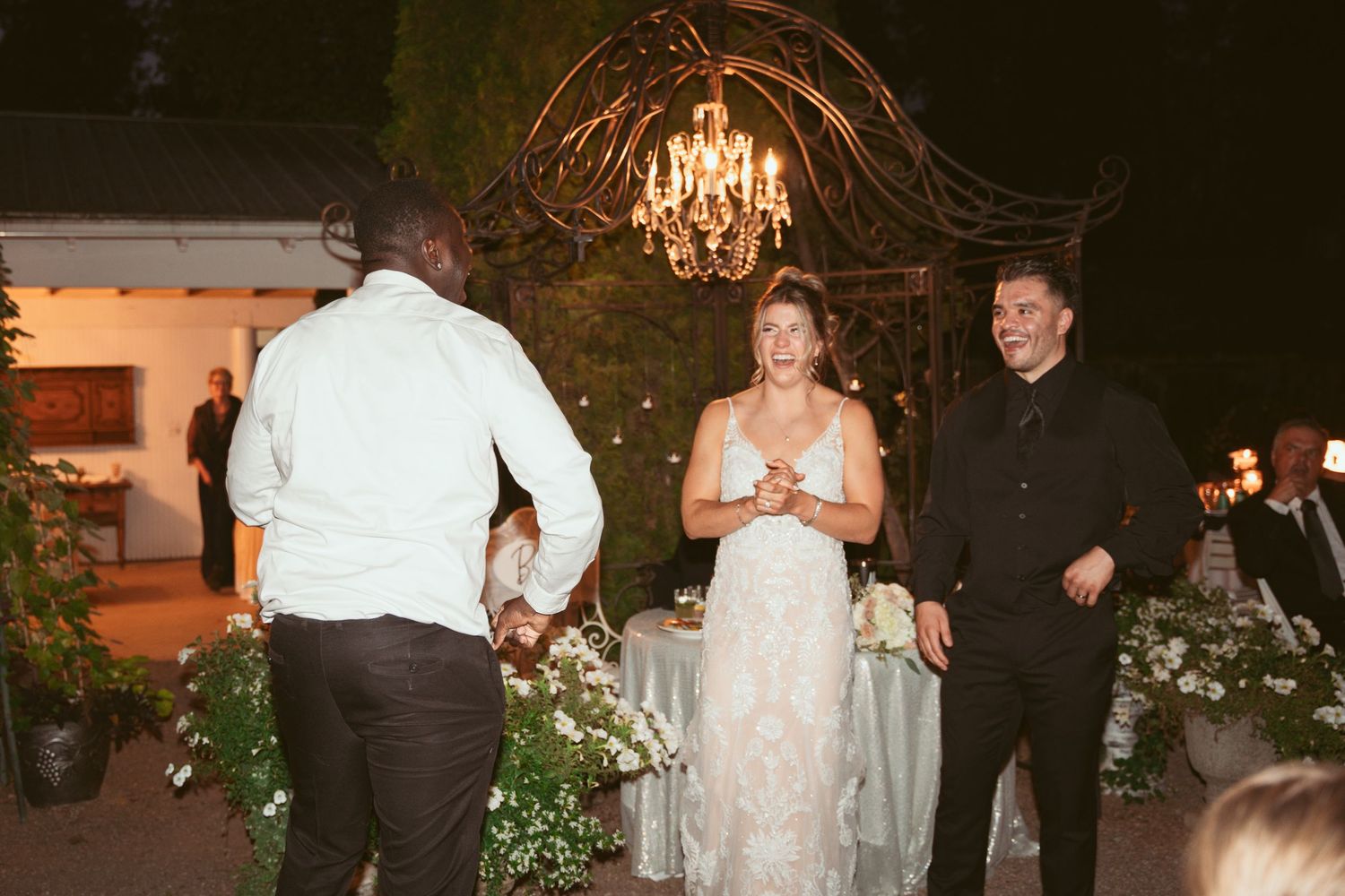 A wedding celebration at an outdoor venue decorated with chandeliers and garden elements.