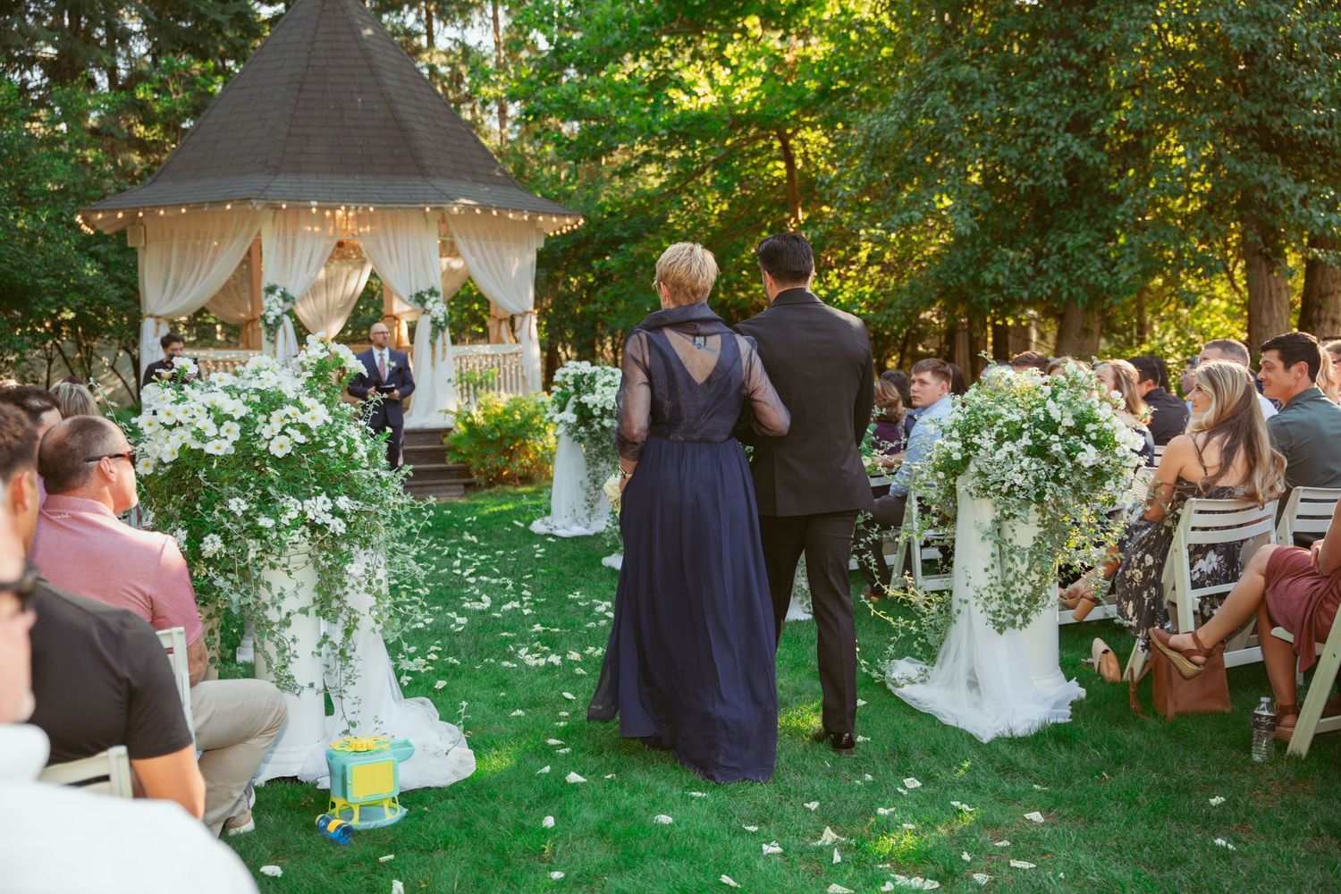 Wedding guests seated on white chairs during an outdoor garden ceremony with lush greenery.