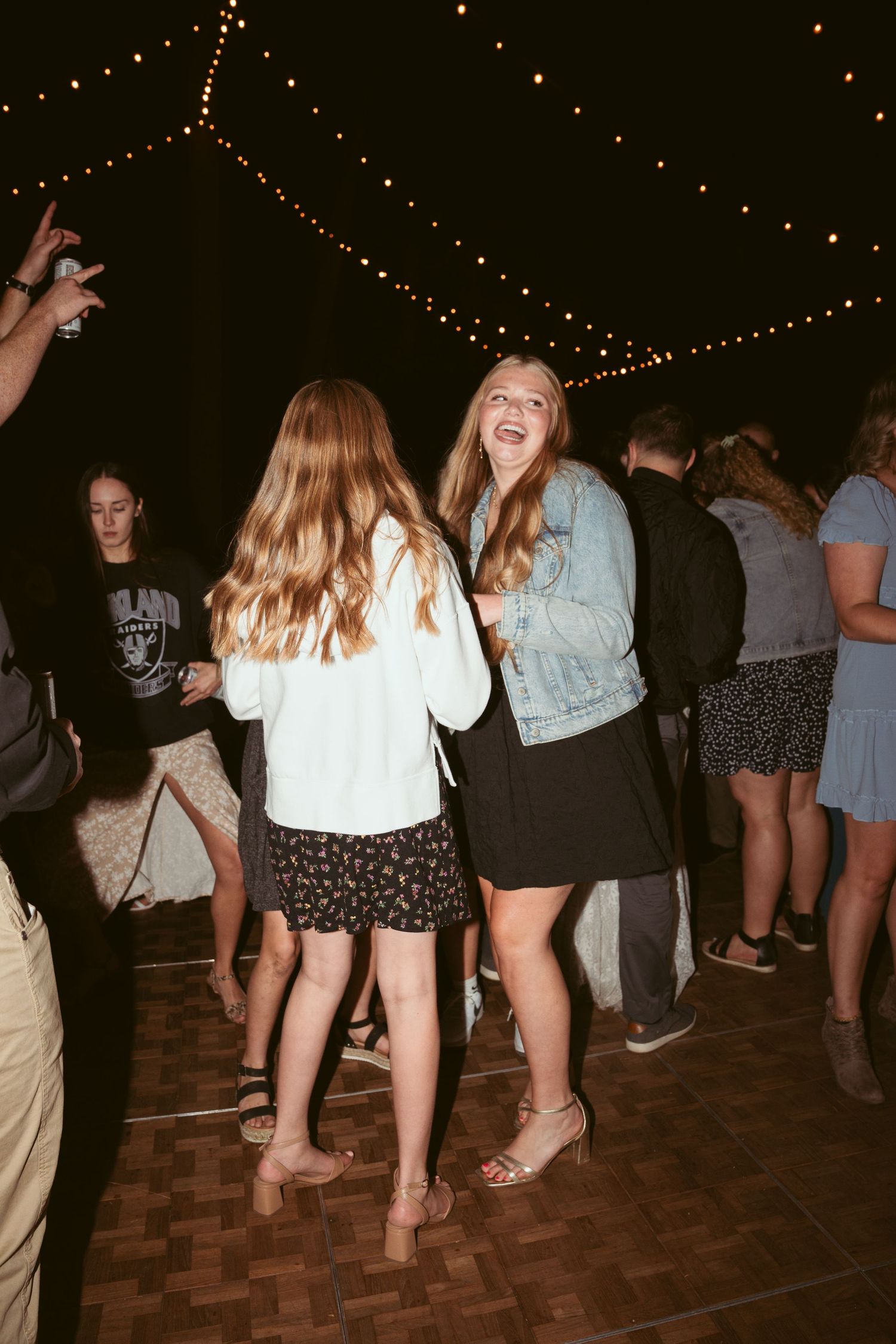 People dancing on a wooden dance floor under string lights at a nighttime wedding reception.