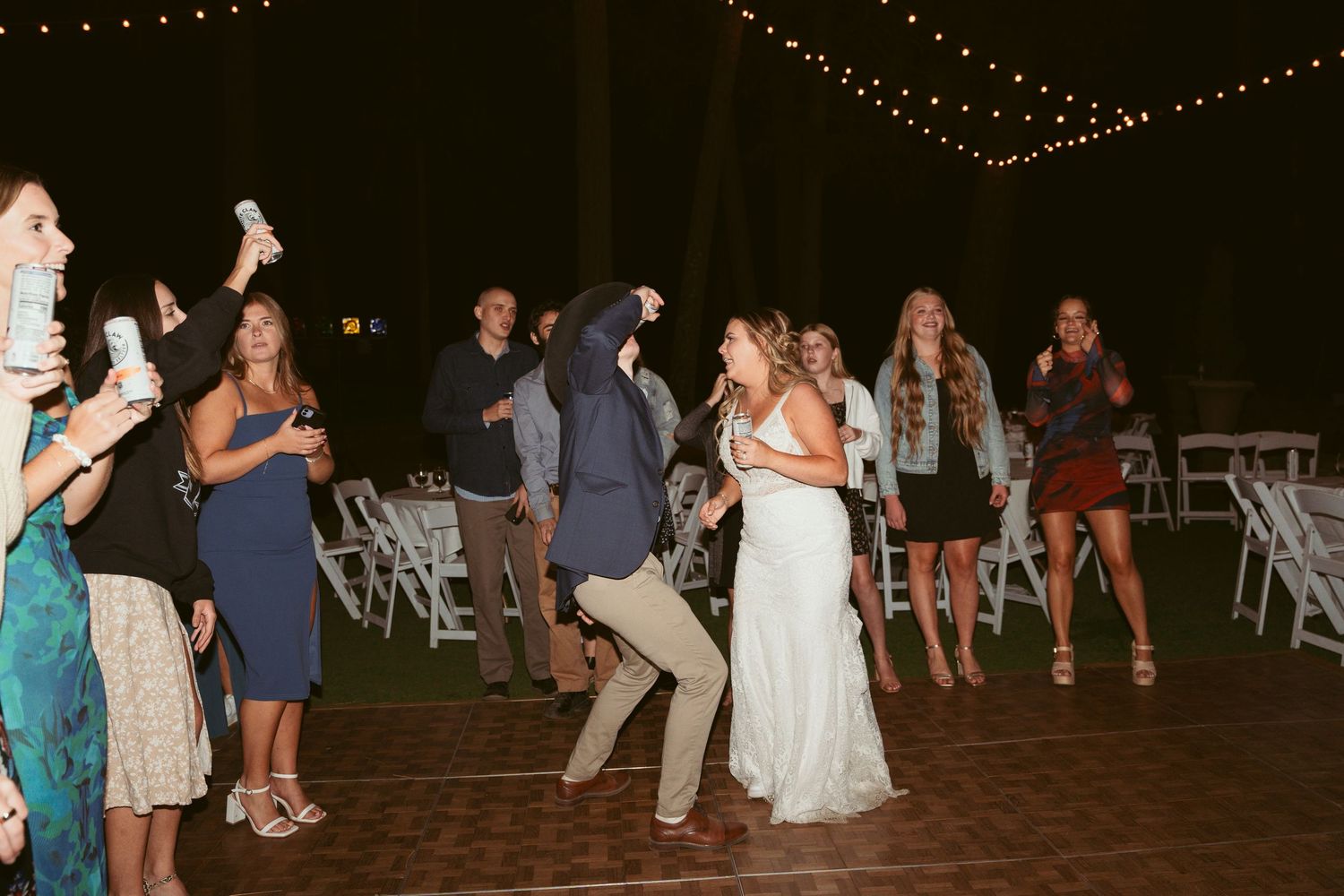 Wedding reception dance floor filled with guests celebrating under string lights.