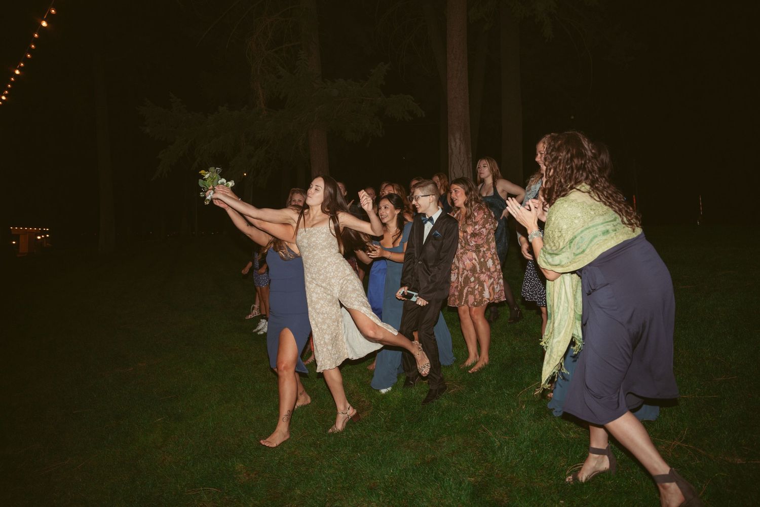 Wedding guests dancing together on a dark dance floor under string lights at an outdoor reception.