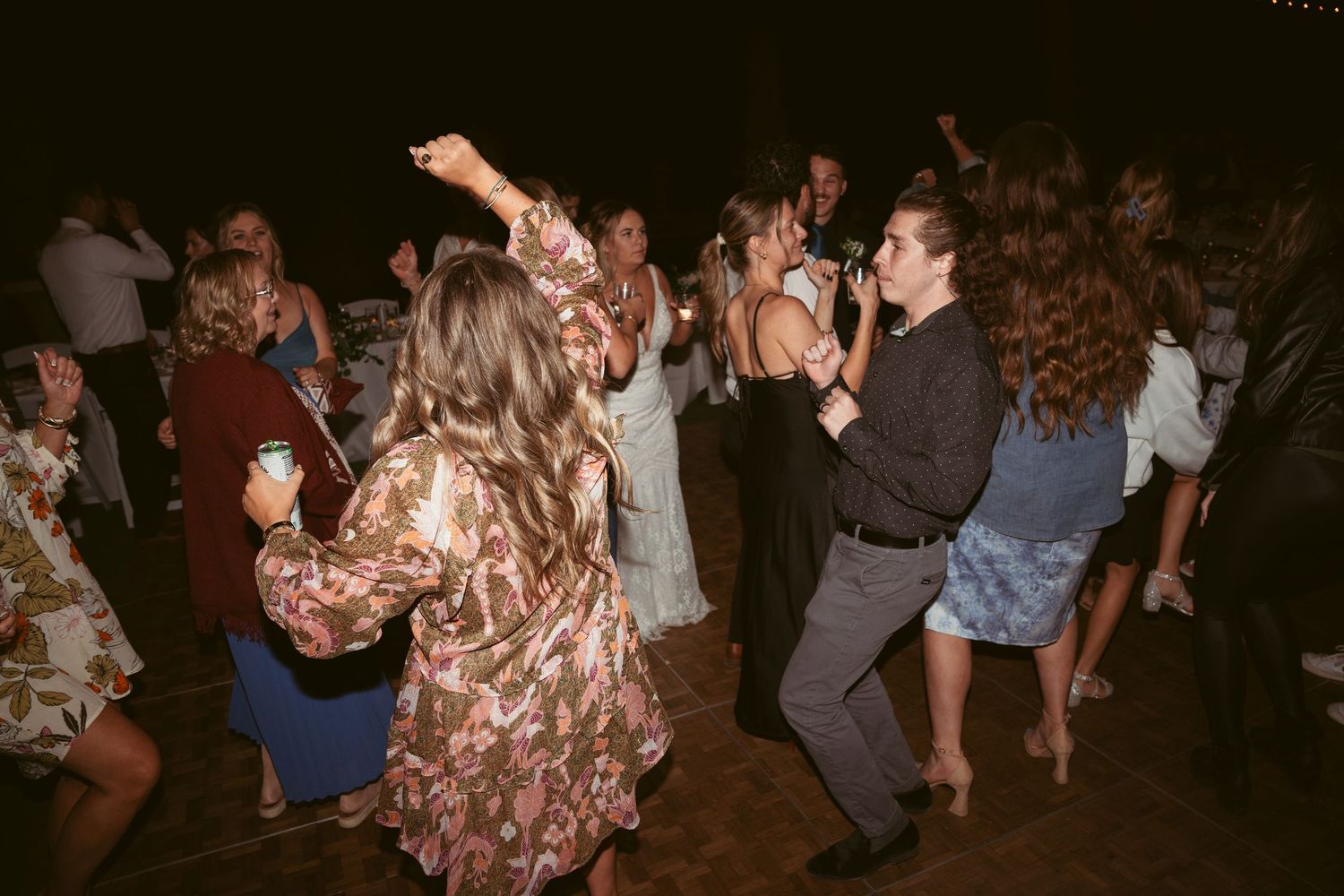 Energetic dancing and celebration under string lights at outdoor wedding reception.