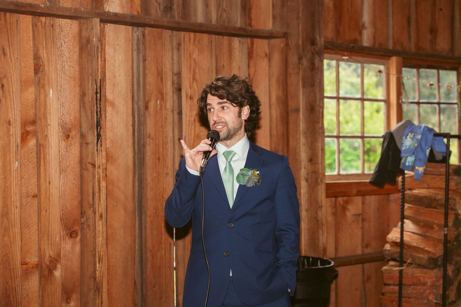 Wedding party members in formal attire standing inside a rustic wooden barn.