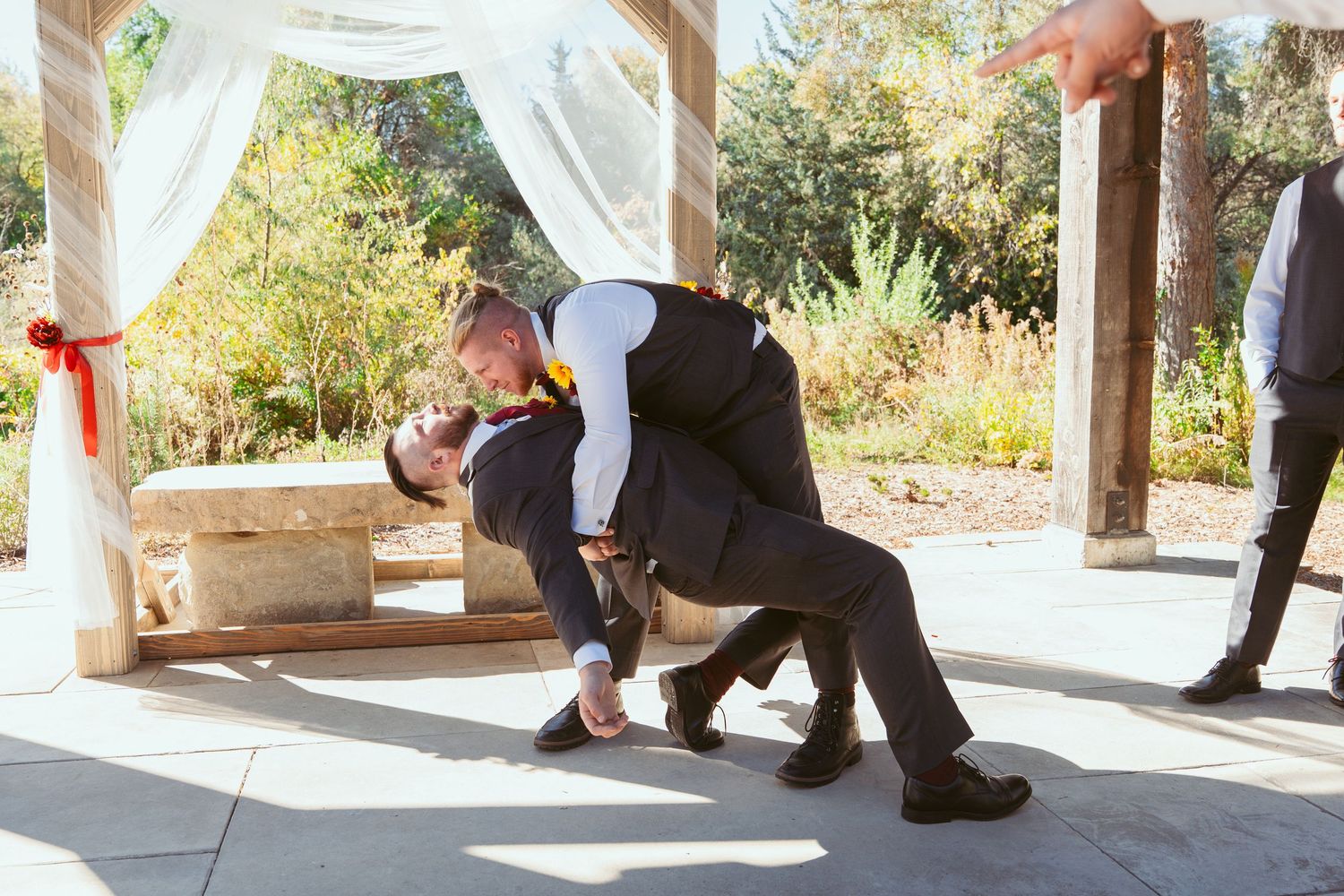 Wedding party members strike dramatic poses under decorated outdoor pavilion.