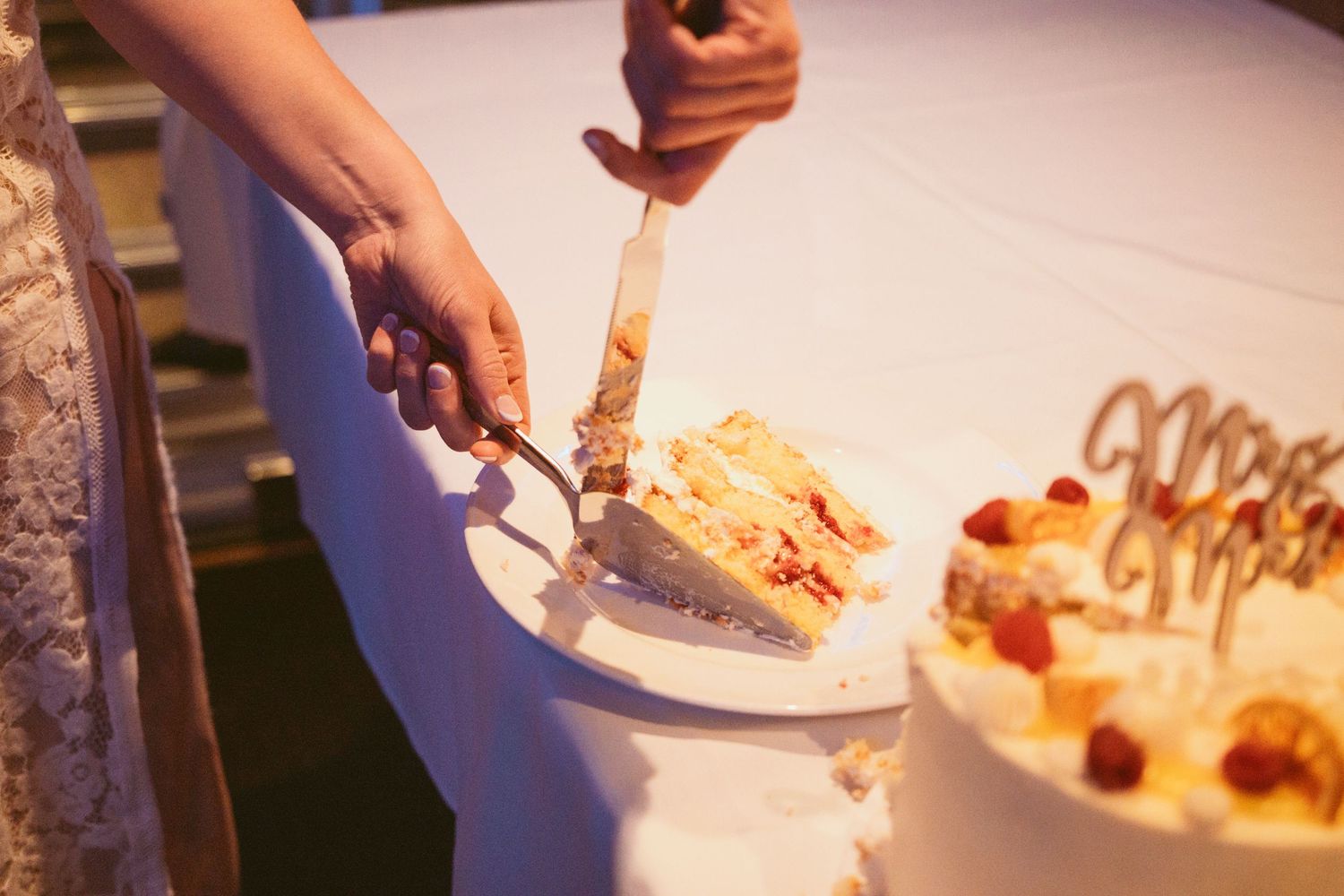 Wedding cake being cut and served on white plates at reception.