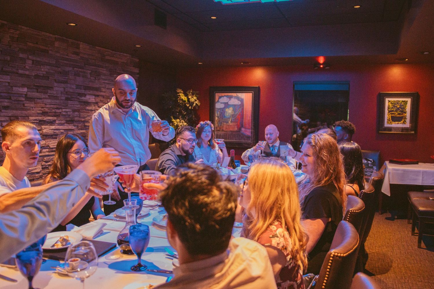 Wedding reception dinner scene with guests toasting at tables in a dimly lit restaurant.