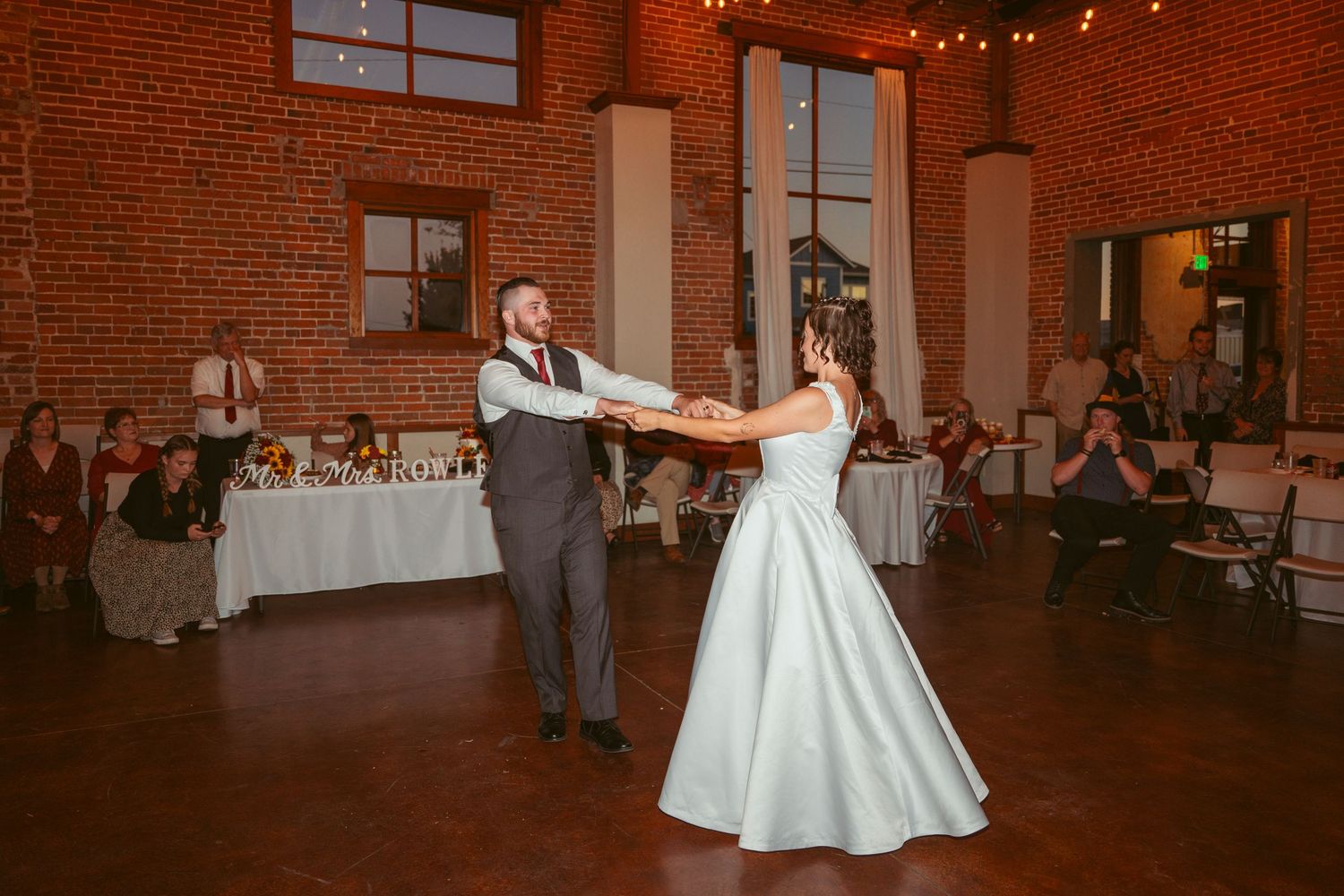 Dancers perform a dramatic spin in an industrial-chic venue with exposed brick and string lights.