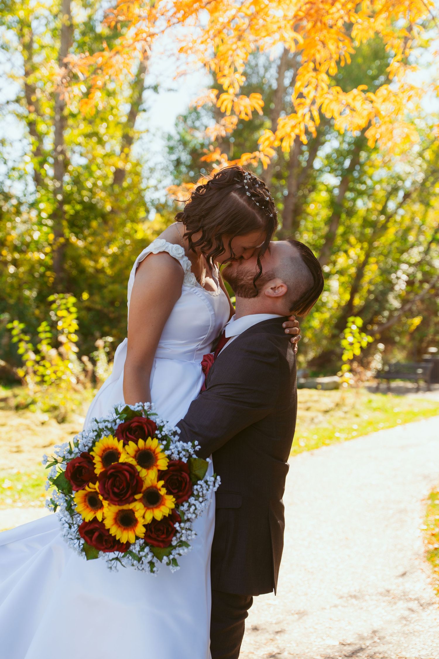 A romantic autumn wedding photo featuring a sunflower bouquet and golden fall foliage.