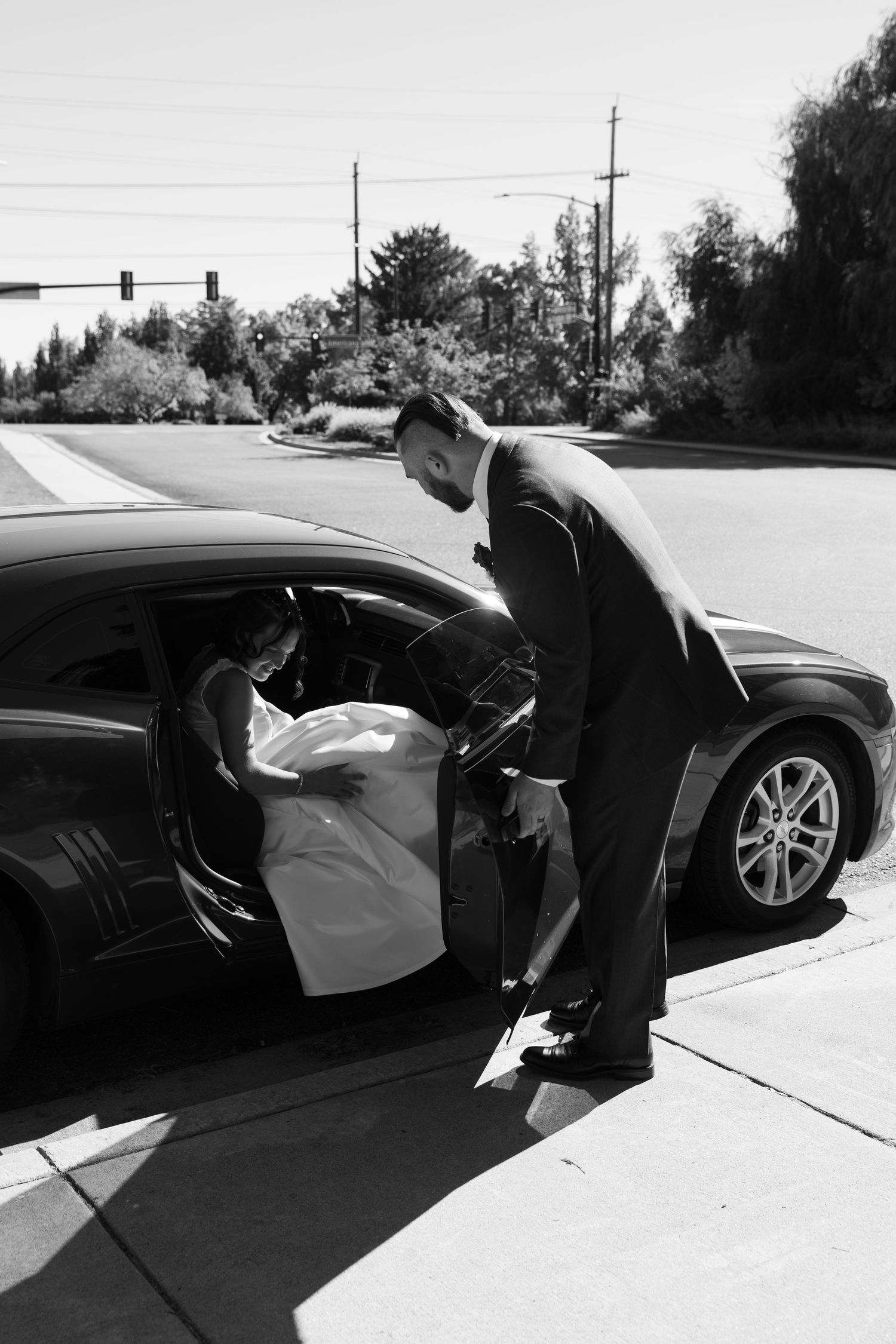 A formal moment captured in black and white as someone helps with a car door.