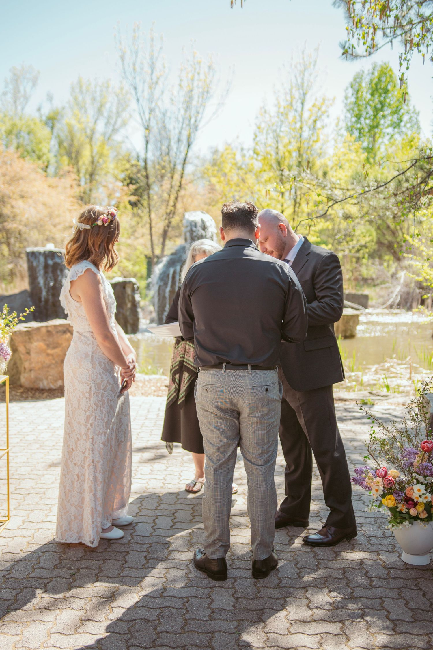 Wedding guests gather on a stone patio during an outdoor ceremony.