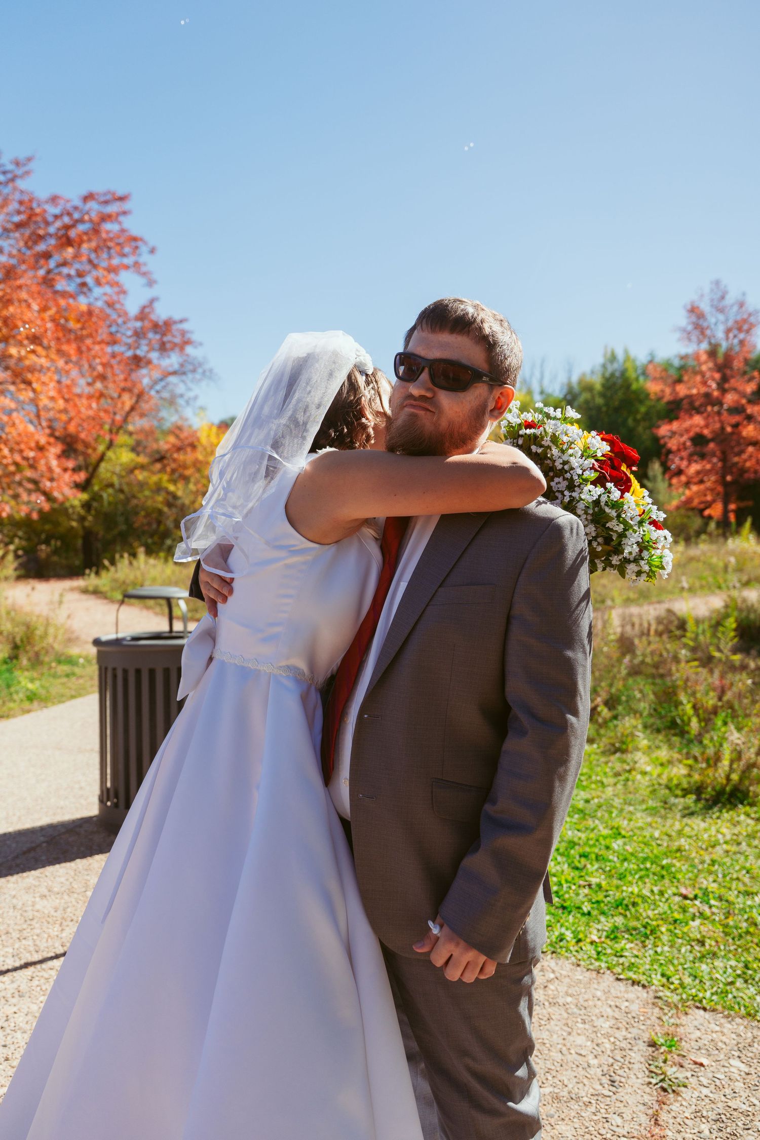 Candid wedding moments captured on scenic autumn path with colorful fall leaves.