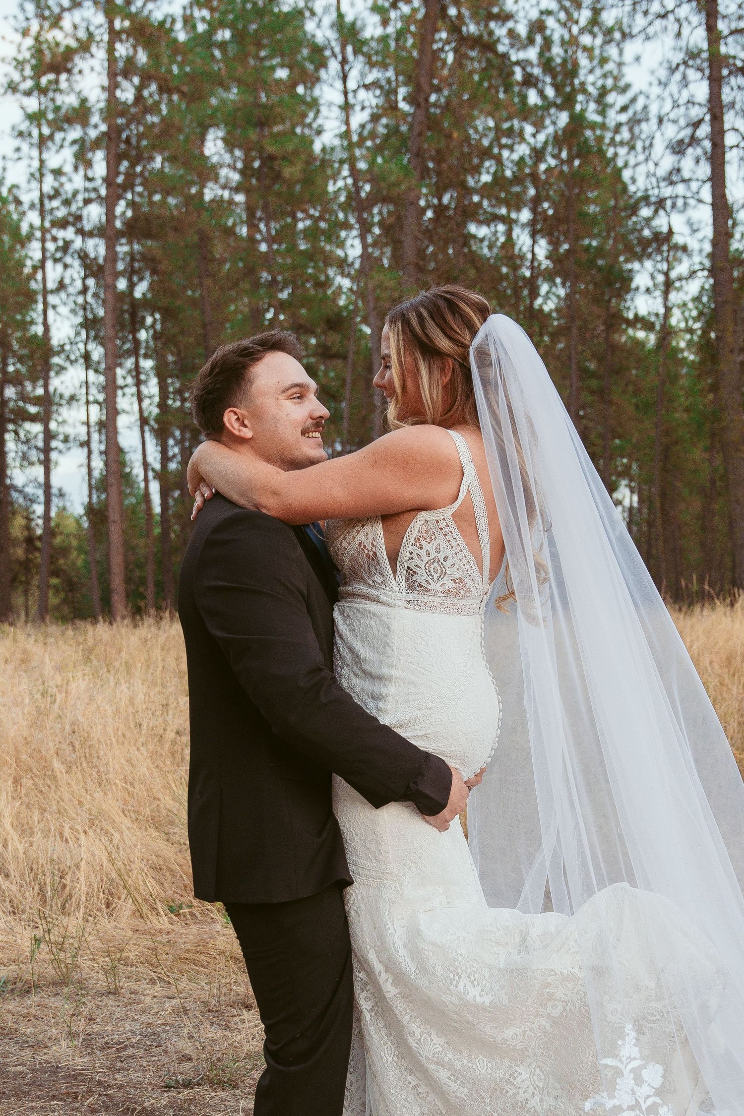 A couple shares a joyful dance moment in a rustic outdoor setting with tall pine trees in the background.