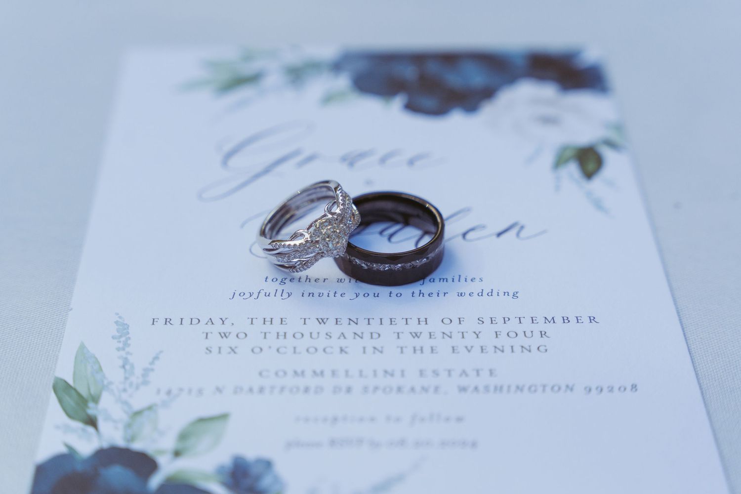 Wedding rings and delicate floral details on white invitation cards create an elegant bridal styling composition.