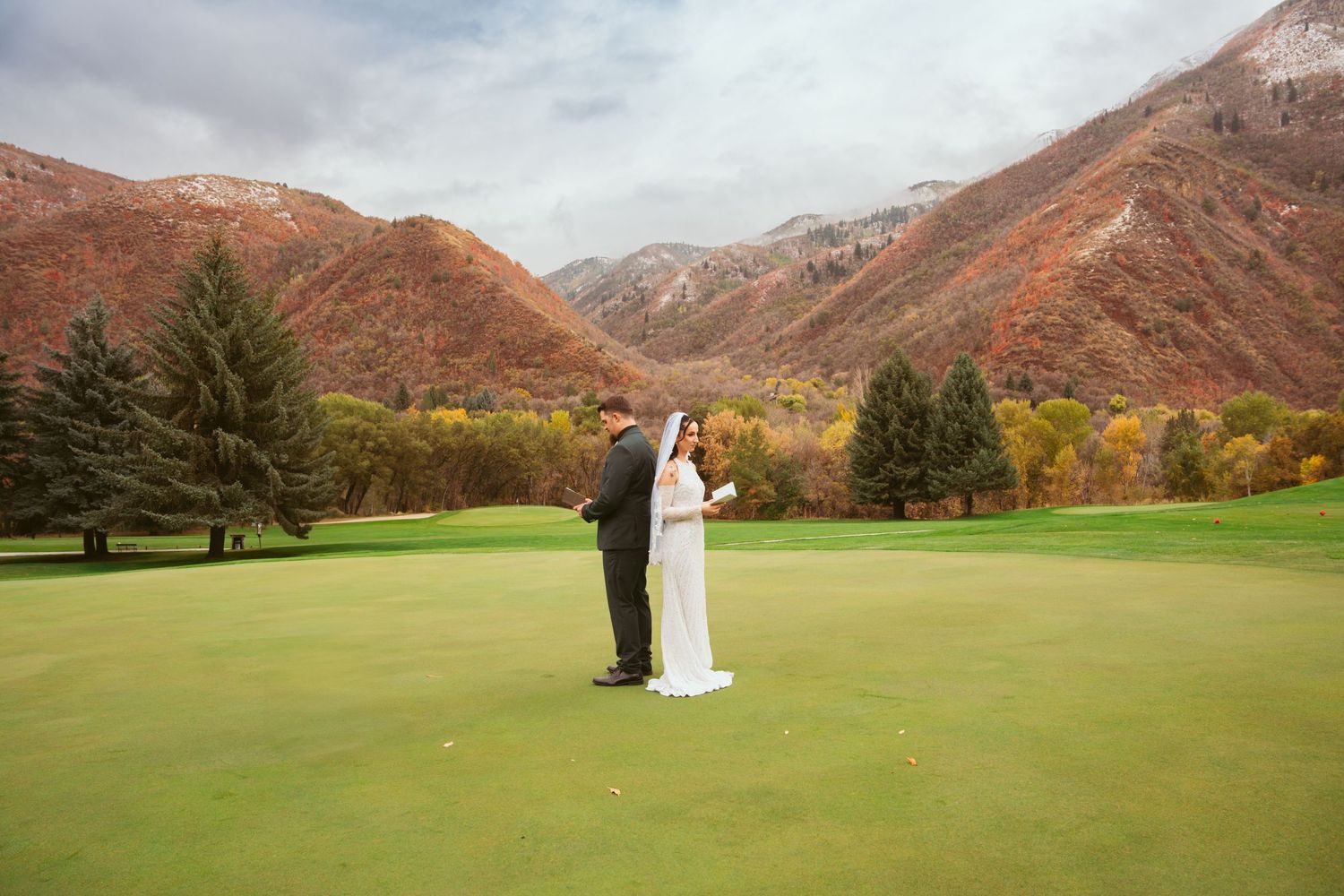 Bride and groom stand on lush green golf course with stunning autumn mountain backdrop in Utah.
