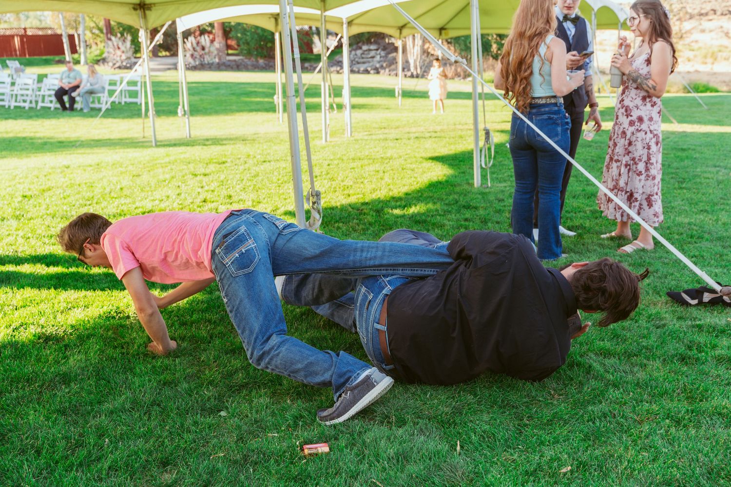 Two people playfully wrestling on green grass at an outdoor event.