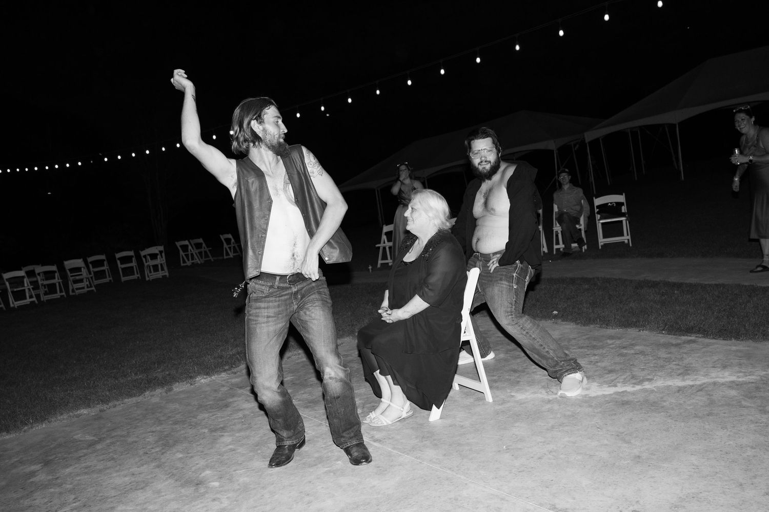 People dancing and celebrating under string lights at nighttime outdoor event.
