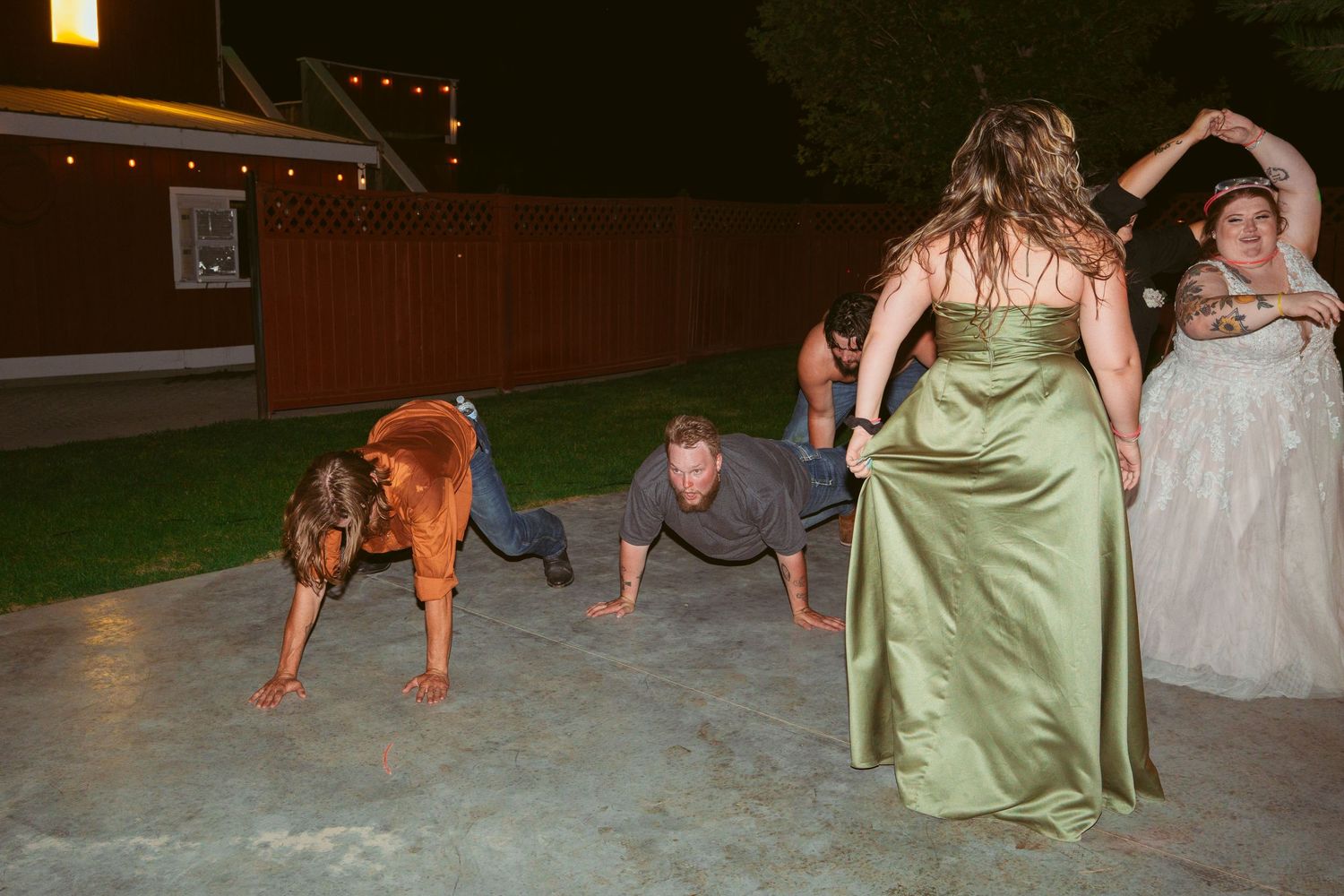 Guests dance and celebrate on a patio during a nighttime wedding reception with string lights overhead.