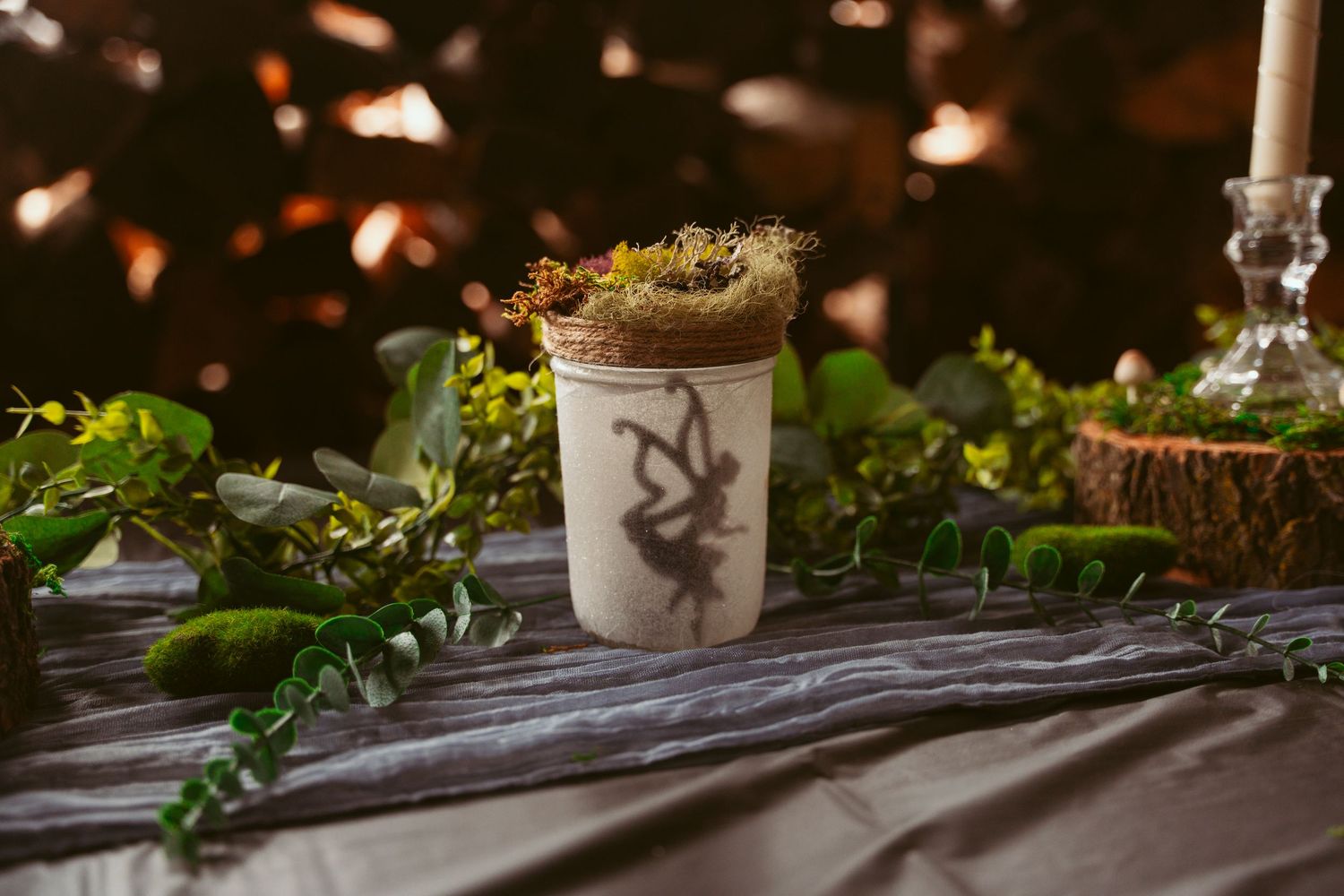 Candlelit table decorations with natural greenery and moss accents for evening reception.