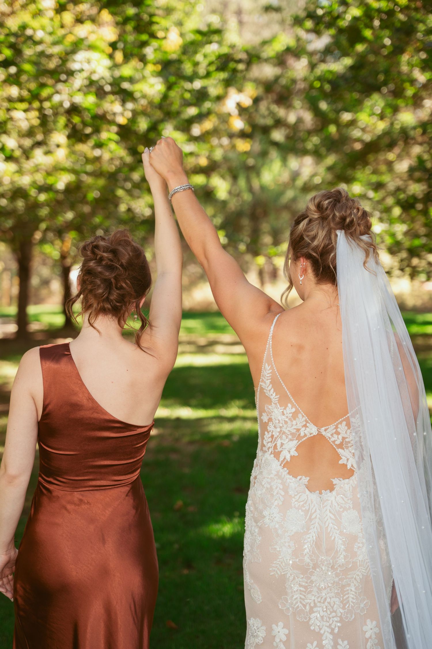 Back view of two people in formal dresses showing off dress details in a sunlit garden setting.